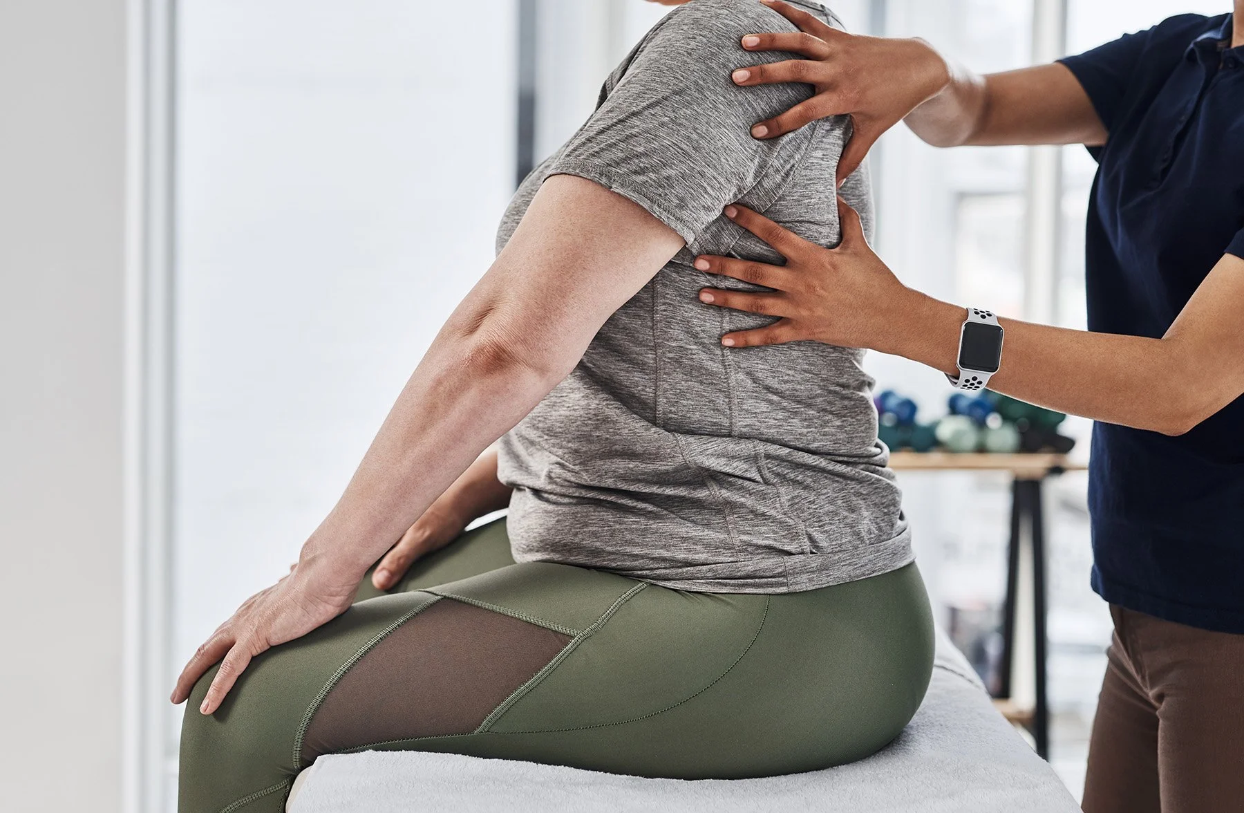 A person receiving physical therapy or chiropractic treatment, sitting on a therapy table, with another person supporting their back and neck.
