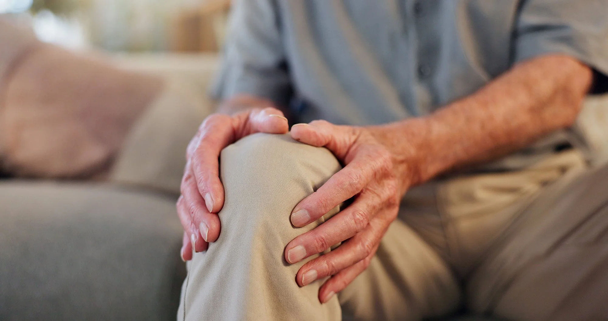 Close-up of elderly person holding their knee with both hands for support.