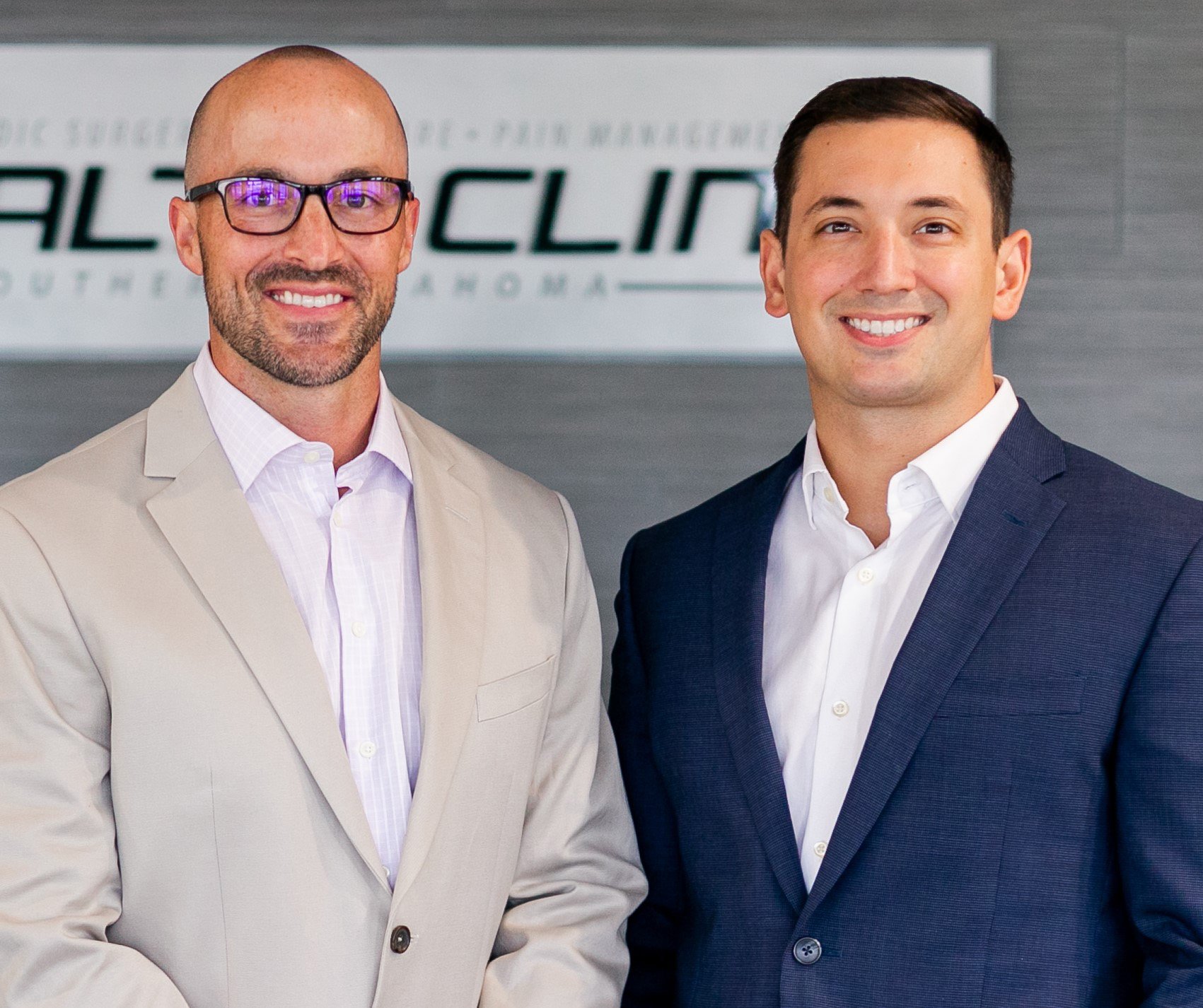 Two men in formal suits are smiling