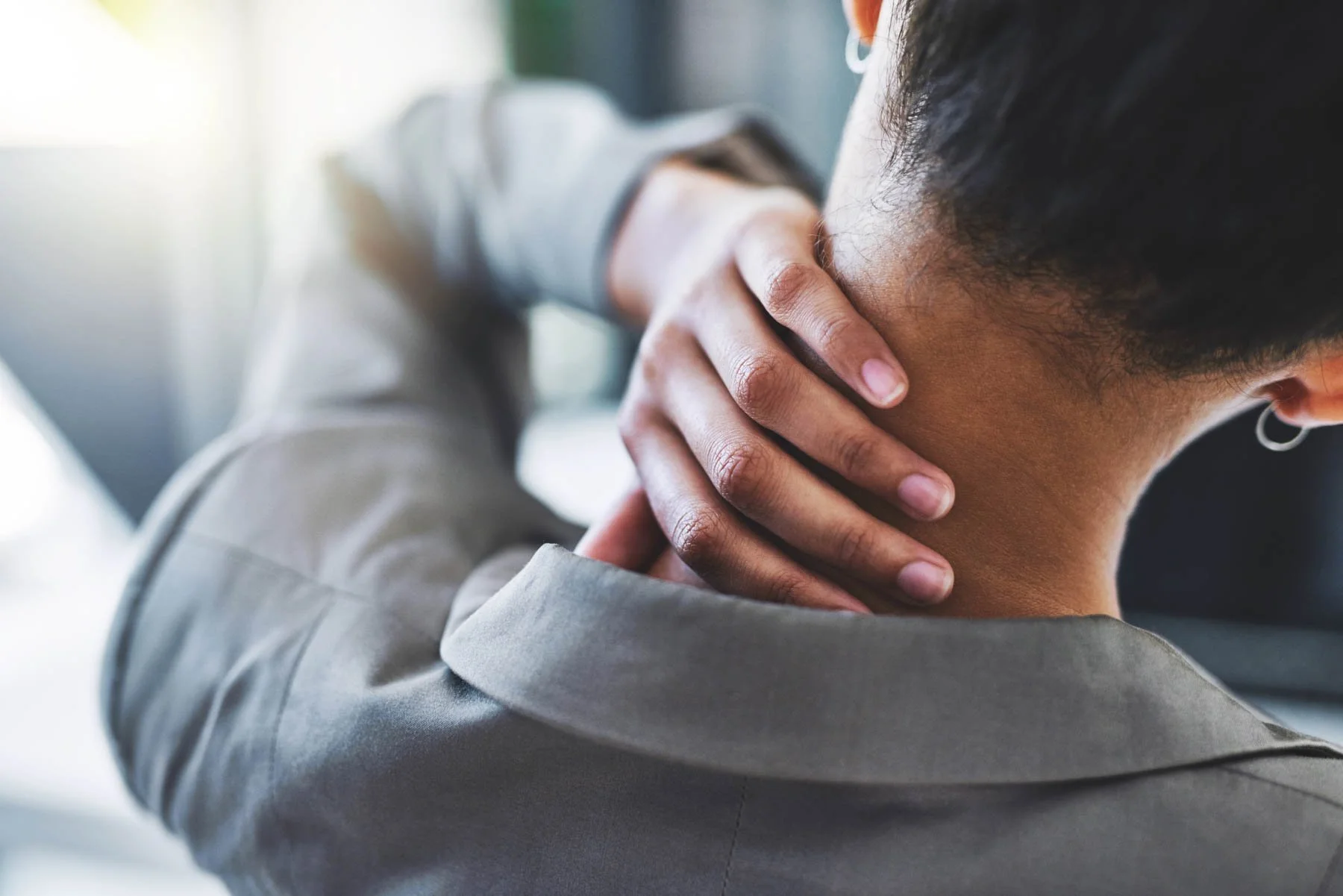 Person holding neck with hand, experiencing neck pain or discomfort, indoors with natural light.