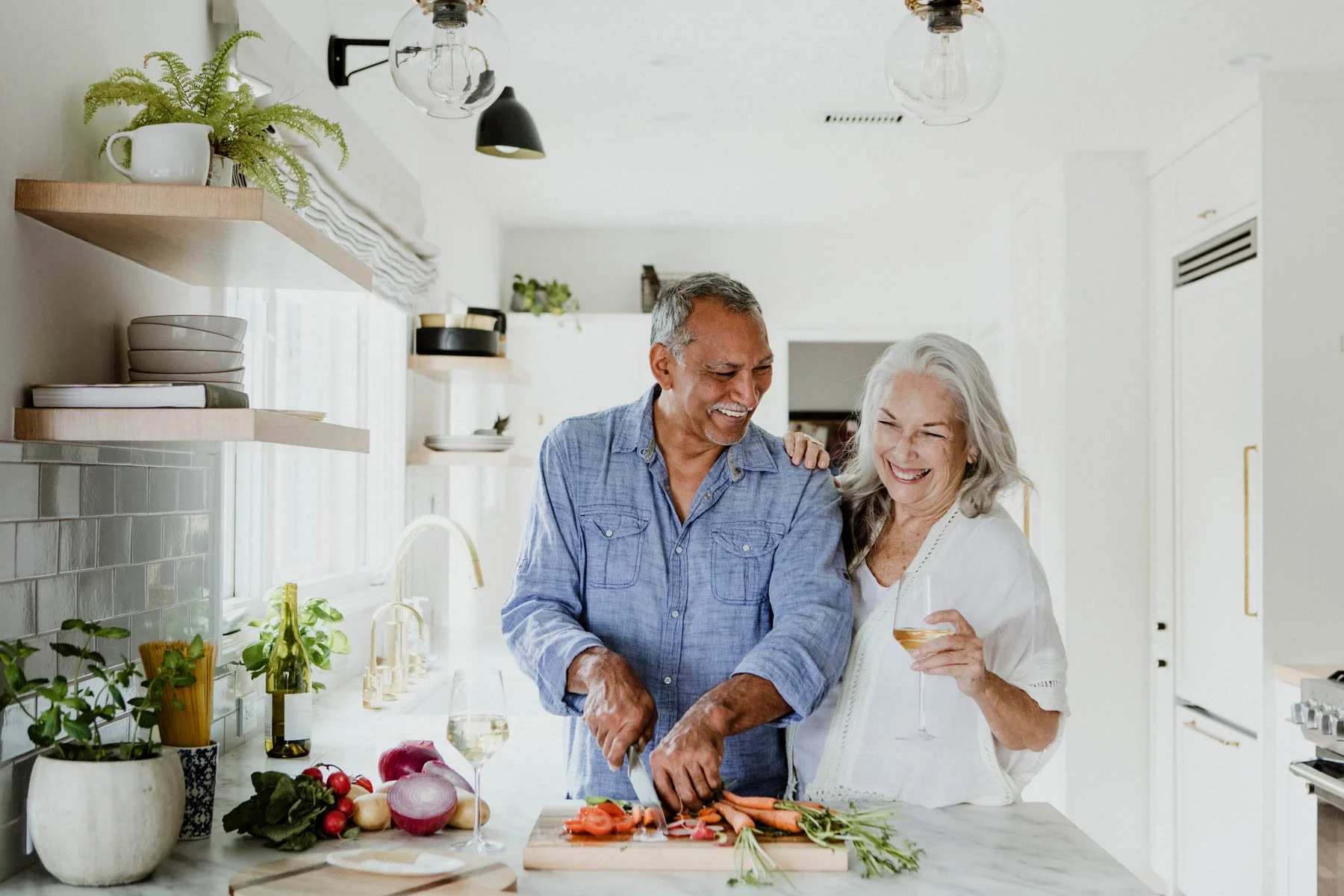 Elderly couple happily cooking together in a bright modern kitchen.