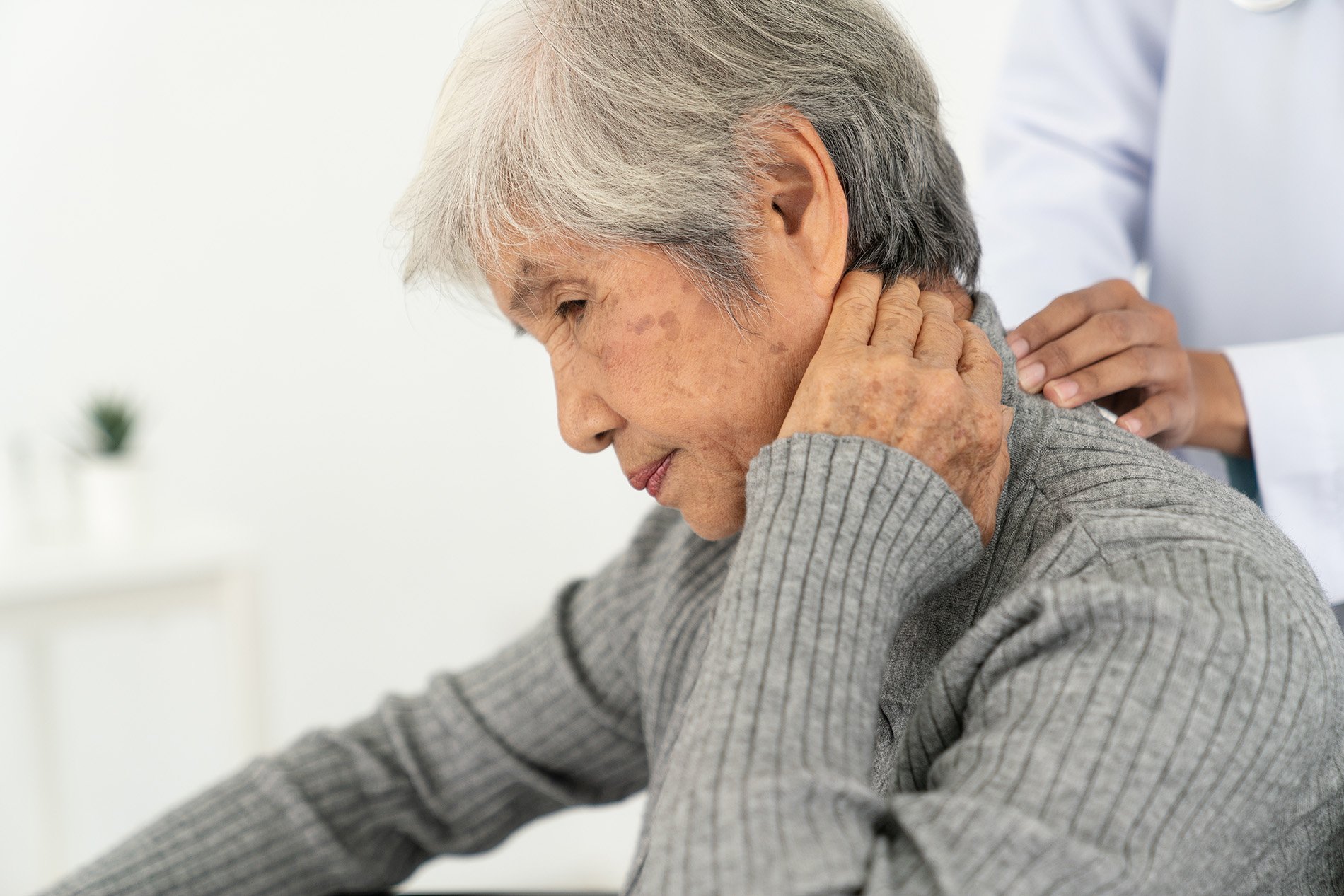 An elderly woman experiencing neck pain while a healthcare professional provides a neck massage.