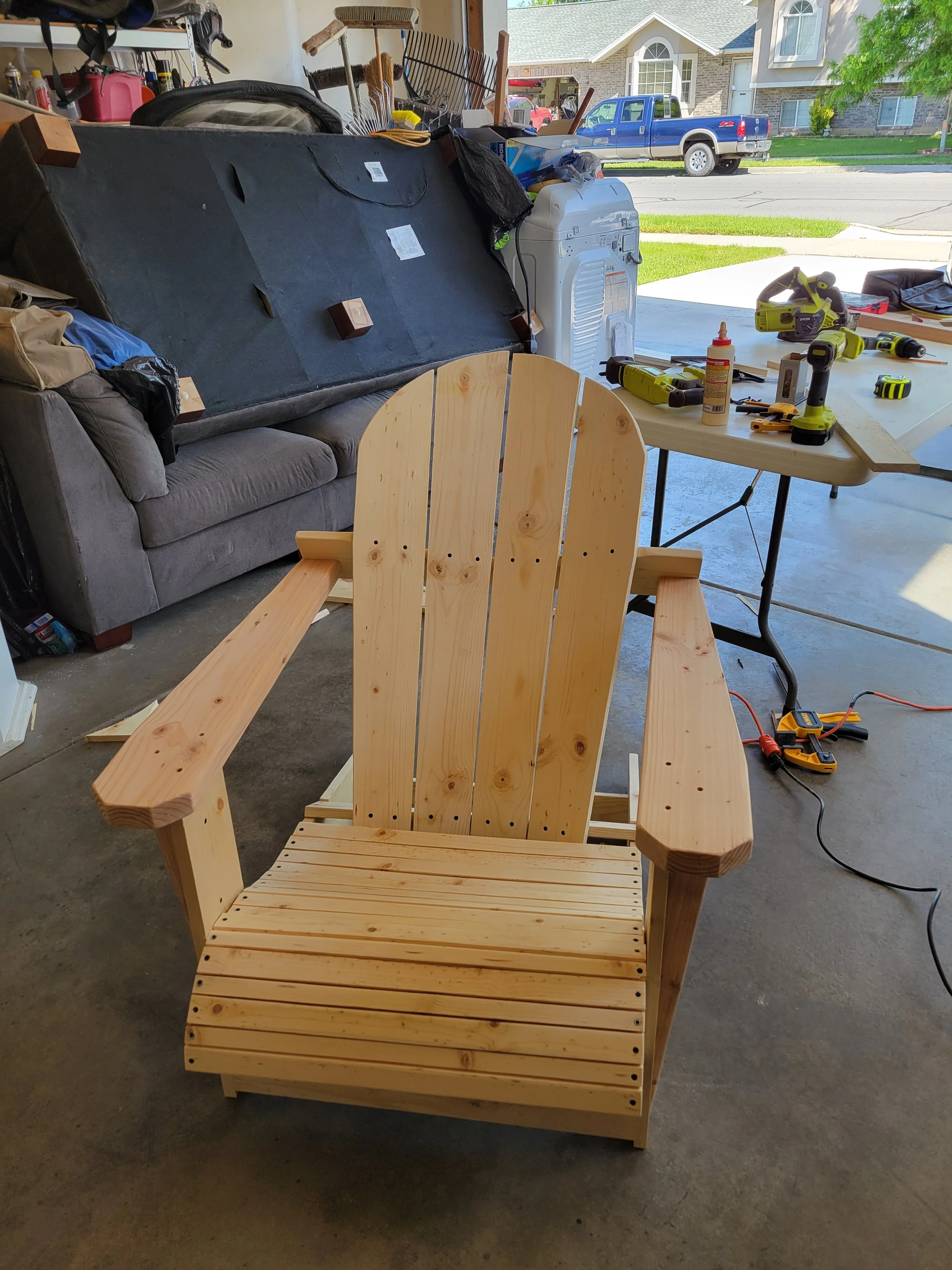 Wooden Adirondack chair in a workshop with tools and a table in the background.