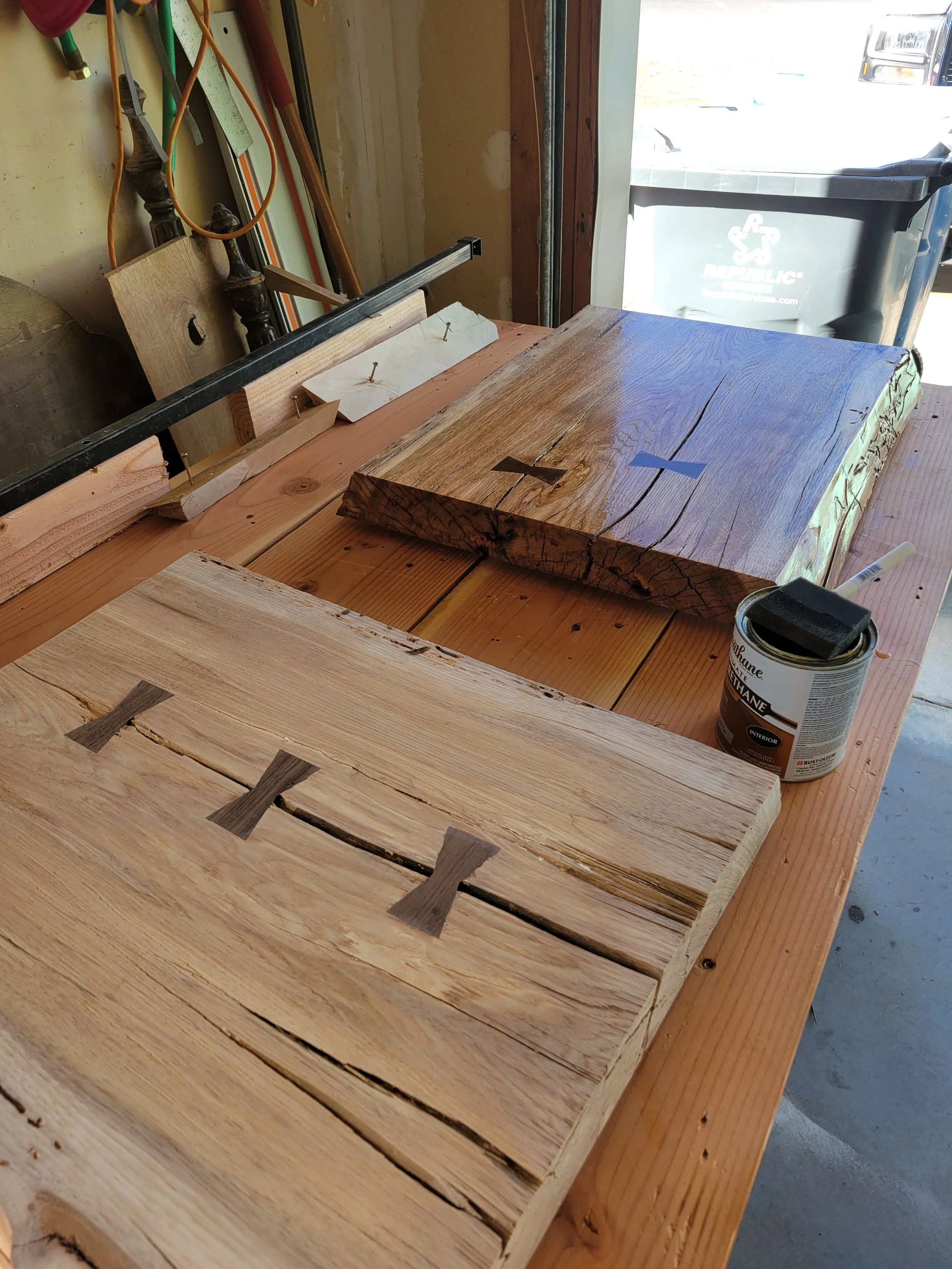 Woodworking workshop with several wooden slabs and clamps on a workbench, along with tools and a can of stain or varnish.