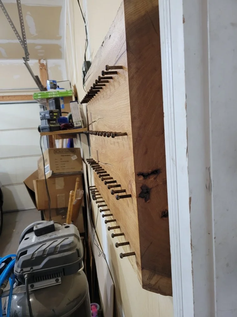 Wooden board with nails protruding, attached to a wall in a workshop or garage.