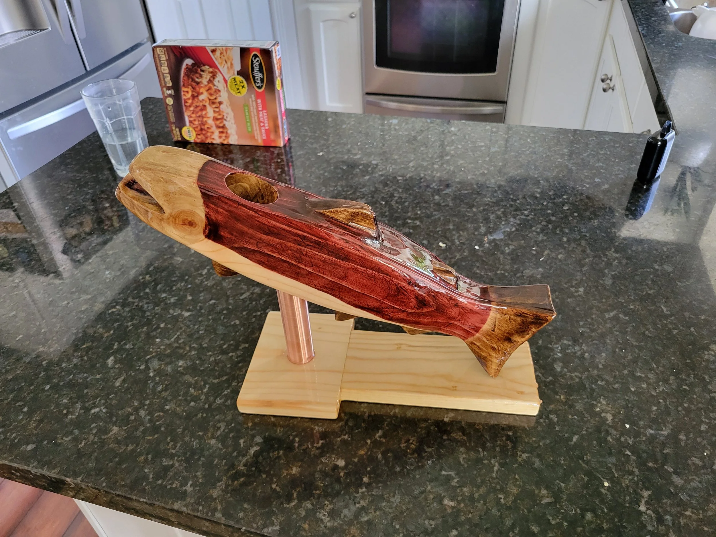 A wooden fish sculpture mounted on a metal stand on a kitchen countertop.