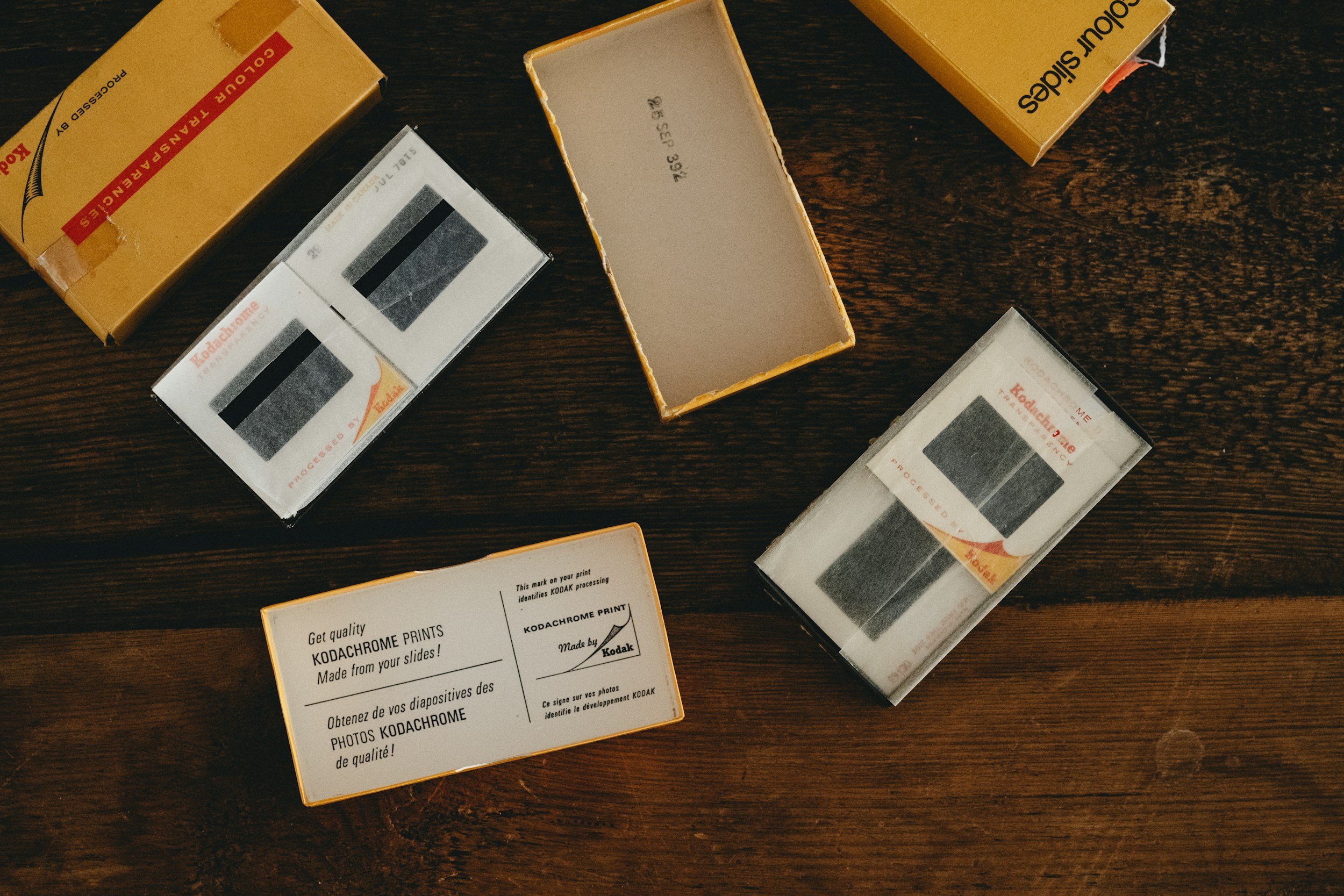 Several boxes of Kodak Kodachrome slide film on a dark wooden surface, some with open lids and labels indicating the brand and product details.