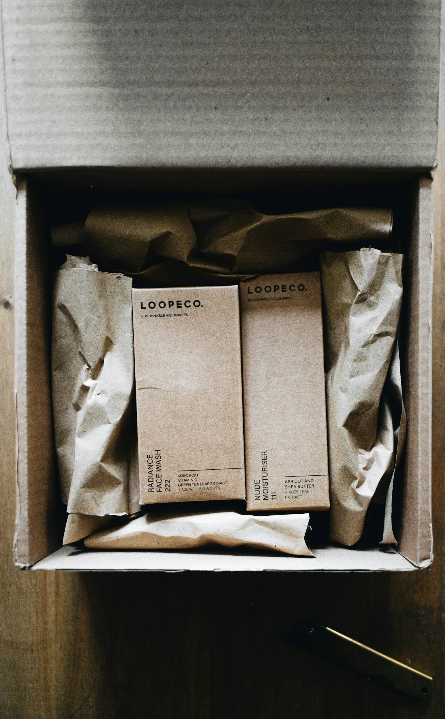 Open cardboard box containing two Loopeco skincare product boxes wrapped in crumpled brown paper.