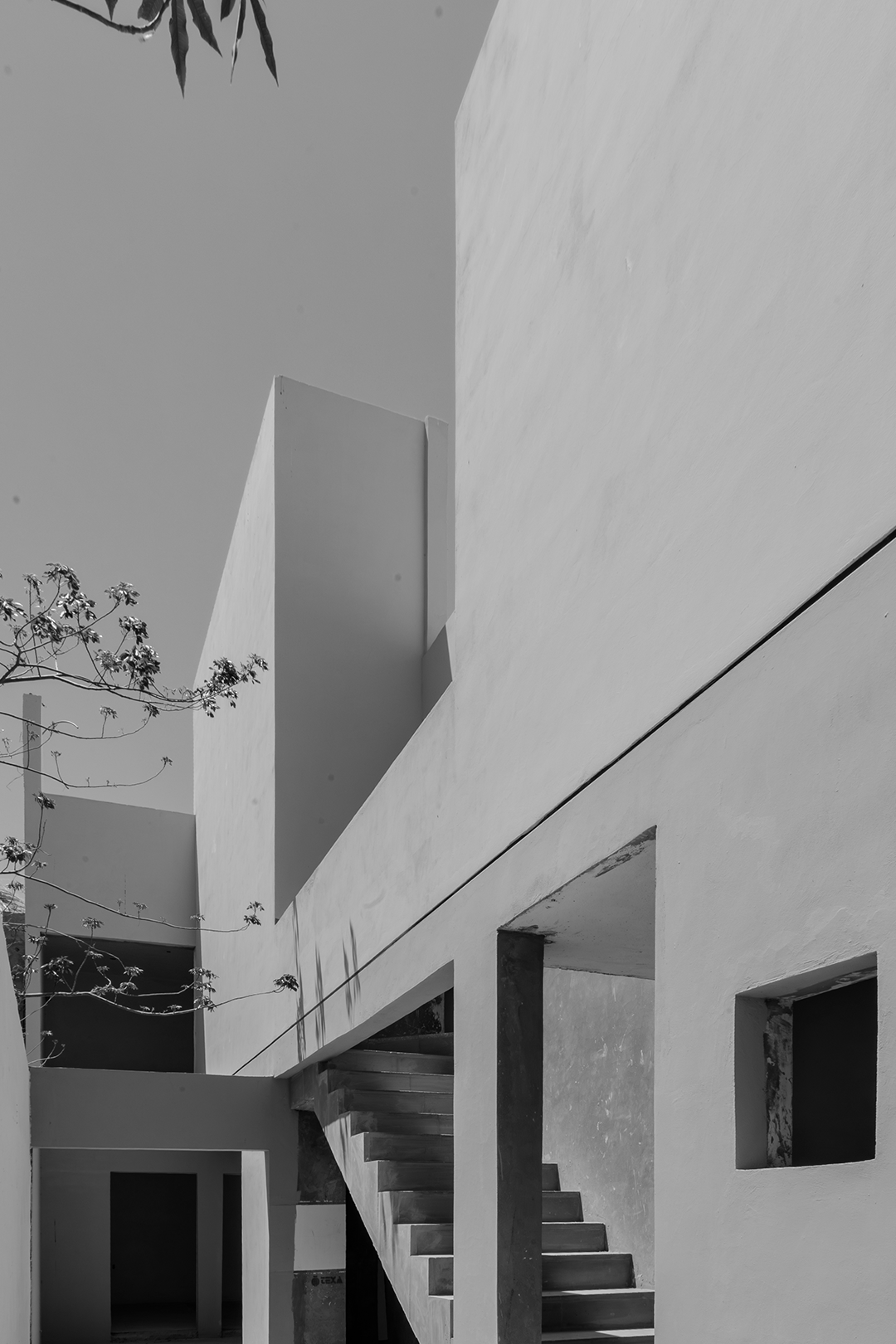 Edificio moderno de paredes blancas y escaleras exteriores, con cielo despejado y rama de árbol en primer plano.