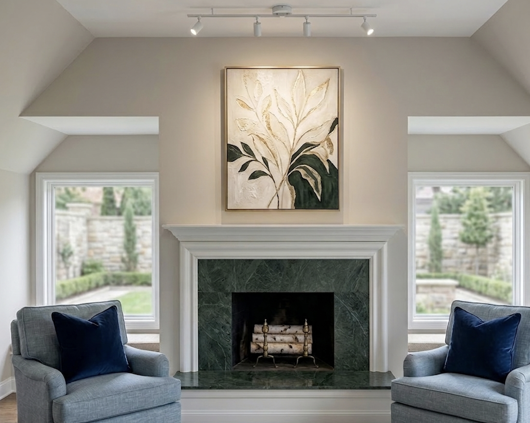 Living room with a fireplace framed in green marble, two blue armchairs with pillows, large windows behind the chairs, and a large framed botanical artwork hanging above the fireplace. The room is well-lit from natural light.