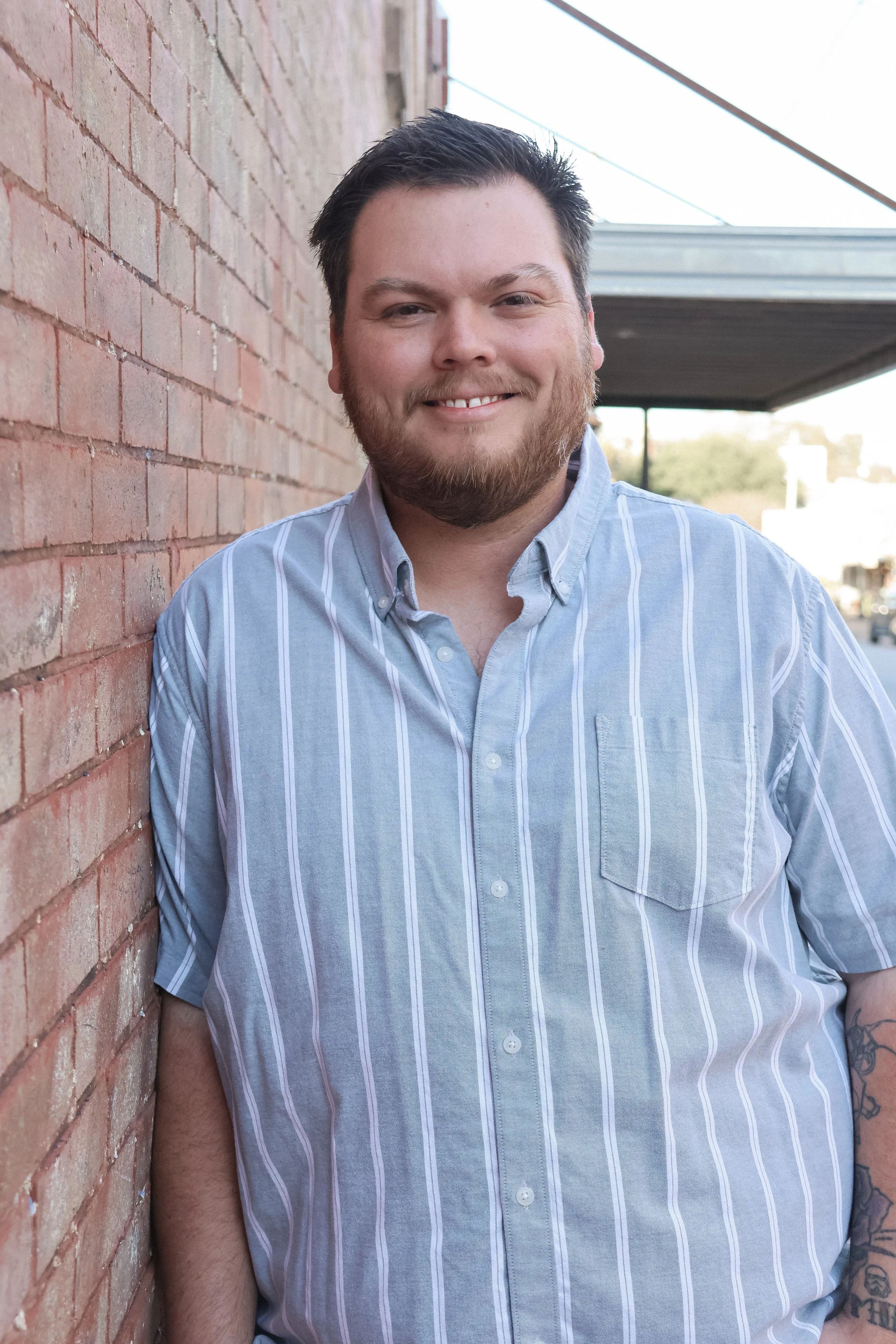 Millett Pools owner, Bryton smiling and leaning against a red brick wall