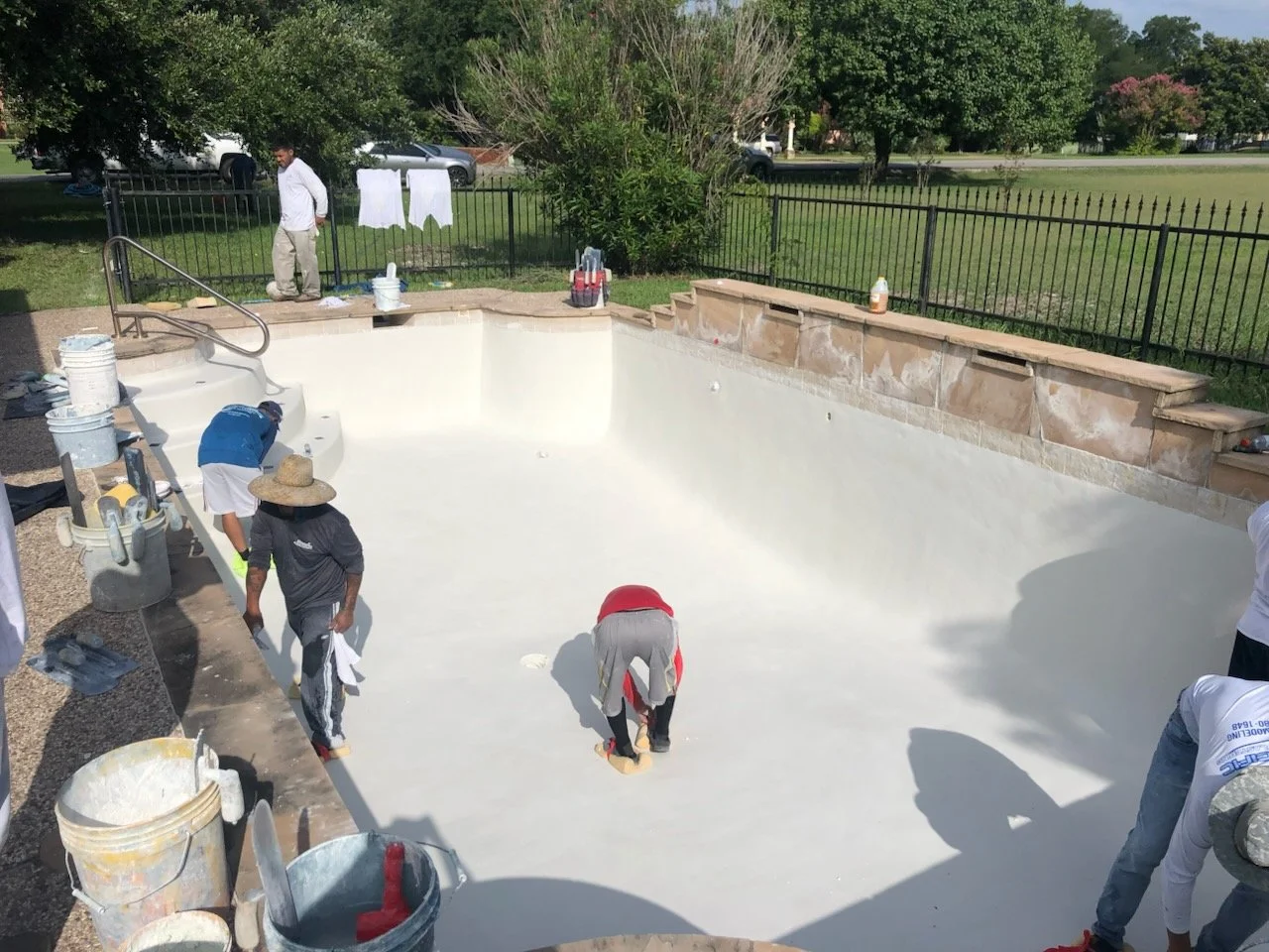 A before-and-after view of a swimming pool renovation, showing an empty, stained pool in the top image and a freshly painted, clean pool in the bottom image, with workers and tools around.