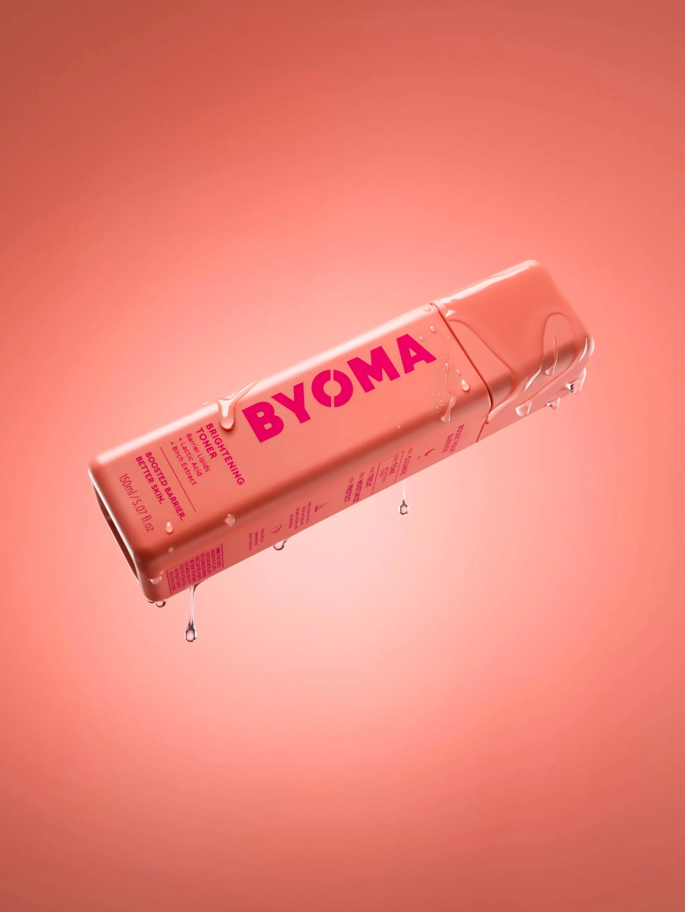 A pink BYOMA skincare product bottle with water droplets on it, floating against a pink background.