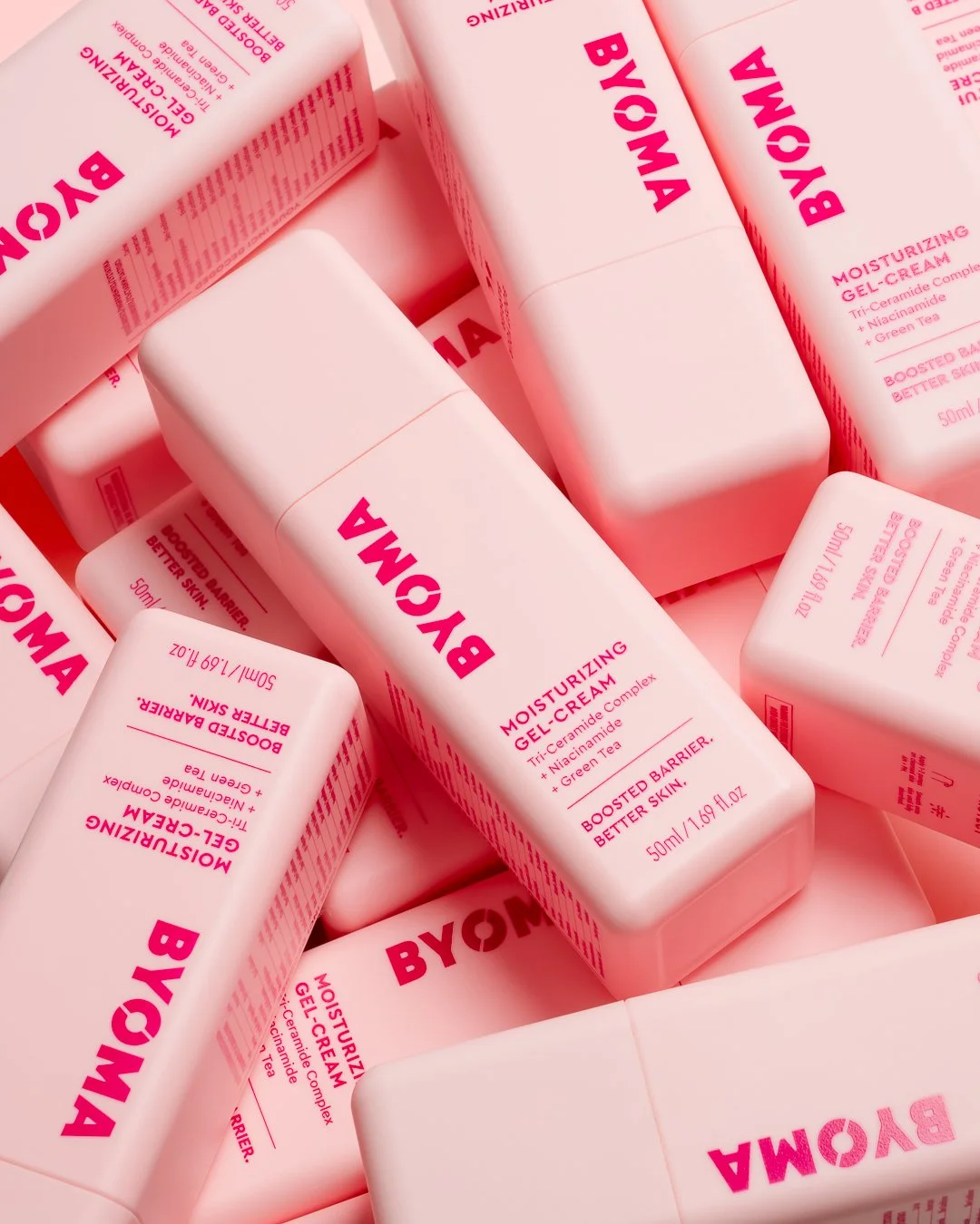 A close-up of multiple pink bottles of BYOMA Moisturizing Gel-Cream arranged in a pile.