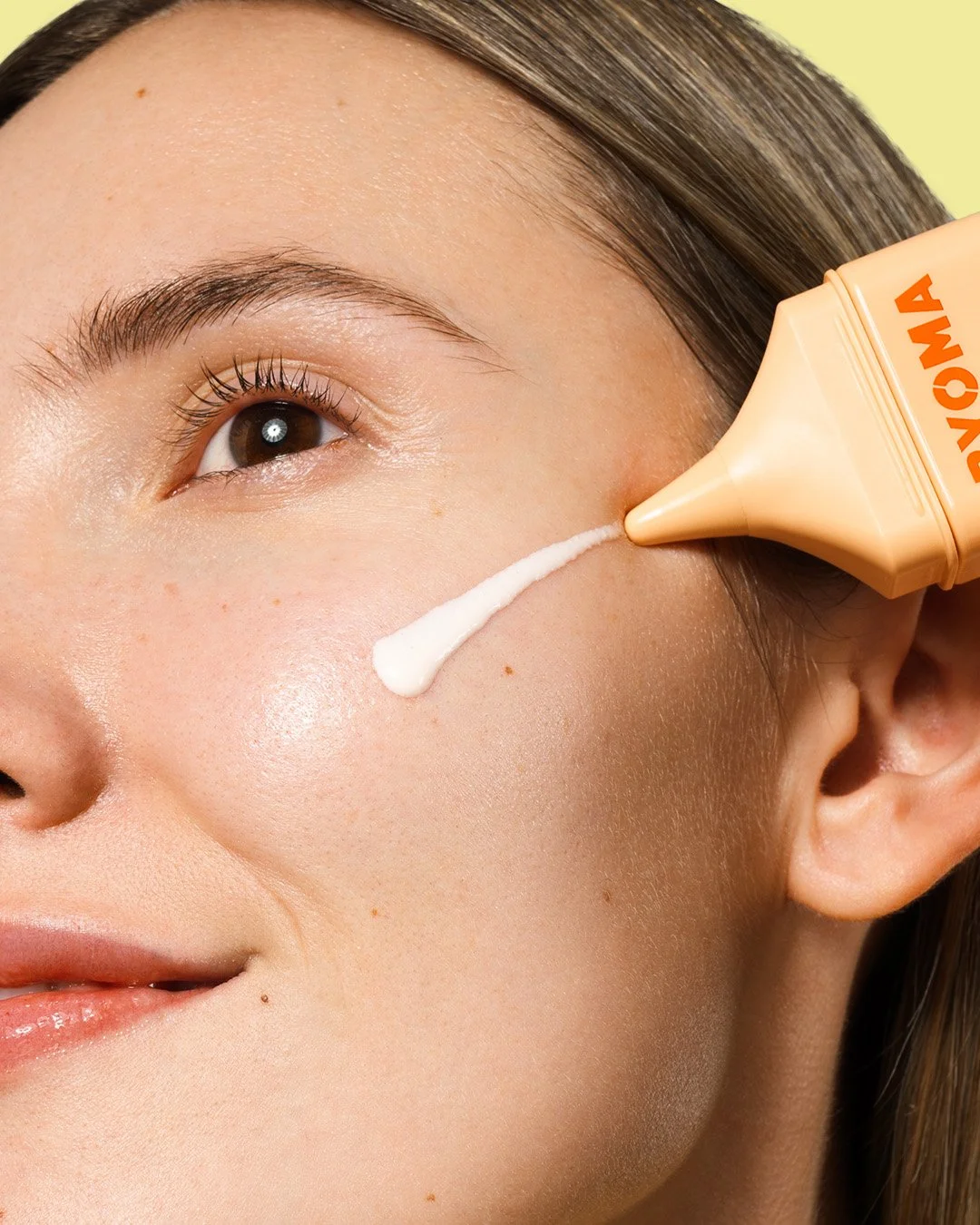 Close-up of a woman's face with a dollop of Kuzova skincare product being applied to her cheek from a squeeze tube.