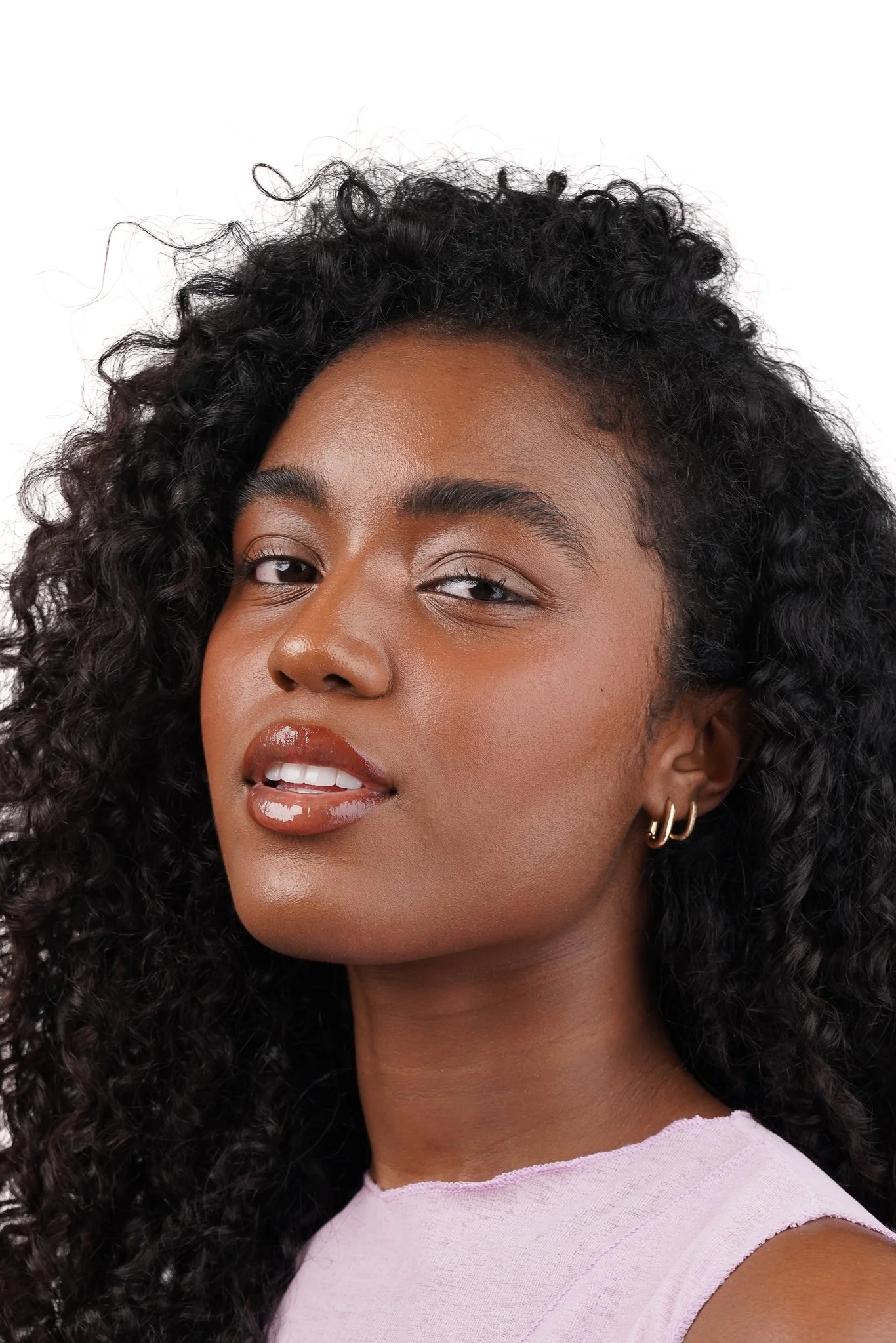 Close-up portrait of a young woman with dark, curly hair, wearing earrings and a light pink top.
