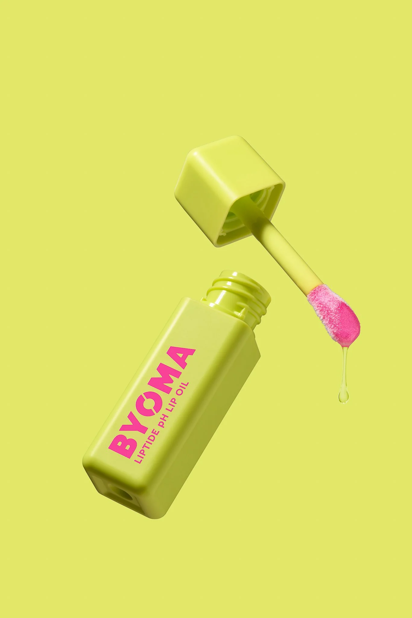 Bright yellow lip gloss bottle labeled 'BYOMA Lip Tides Lip Oil' with pink doe-foot applicator and a droplet of oil, set against a yellow background.