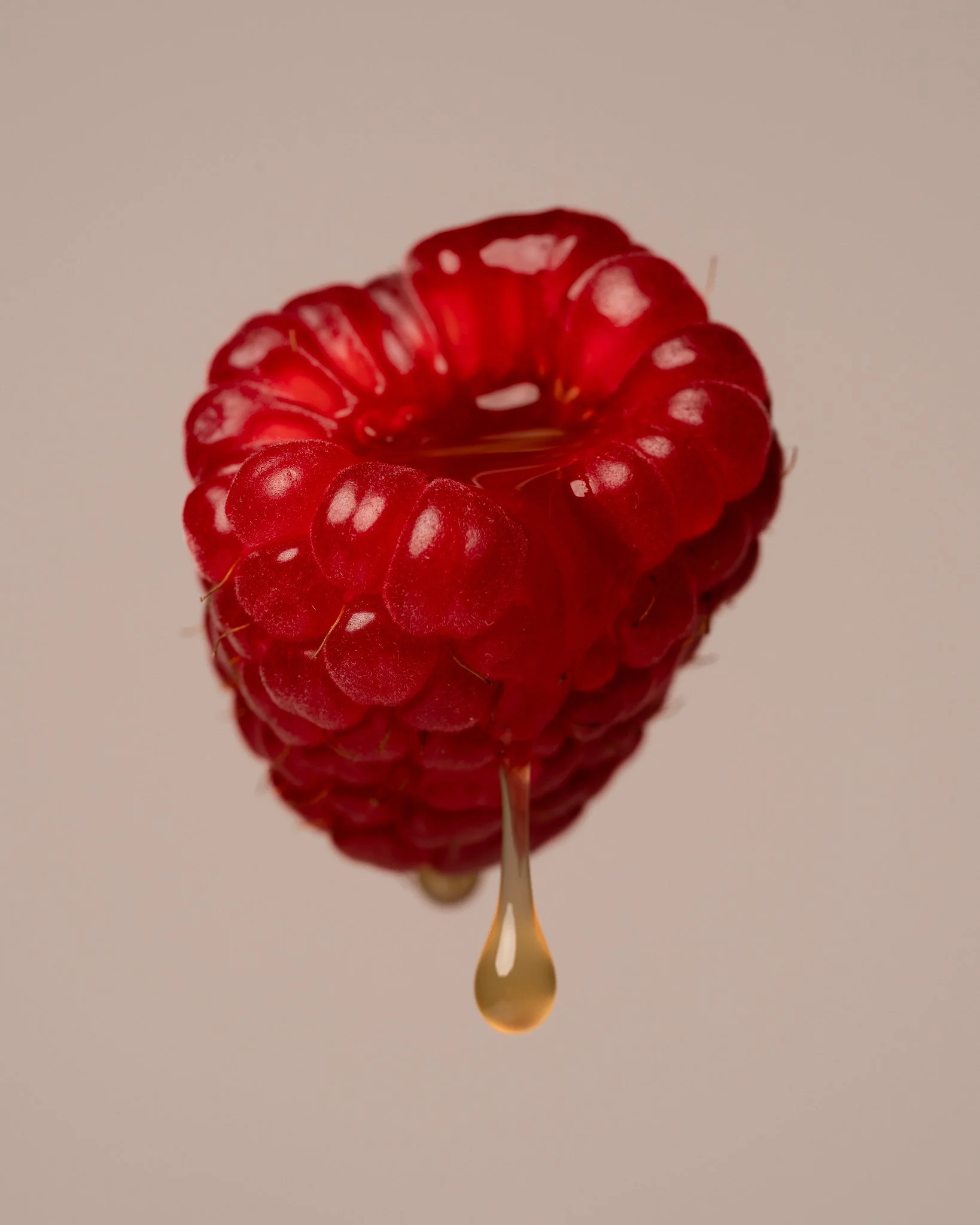 Close-up of a ripe red raspberry with honey drip hanging from its bottom.