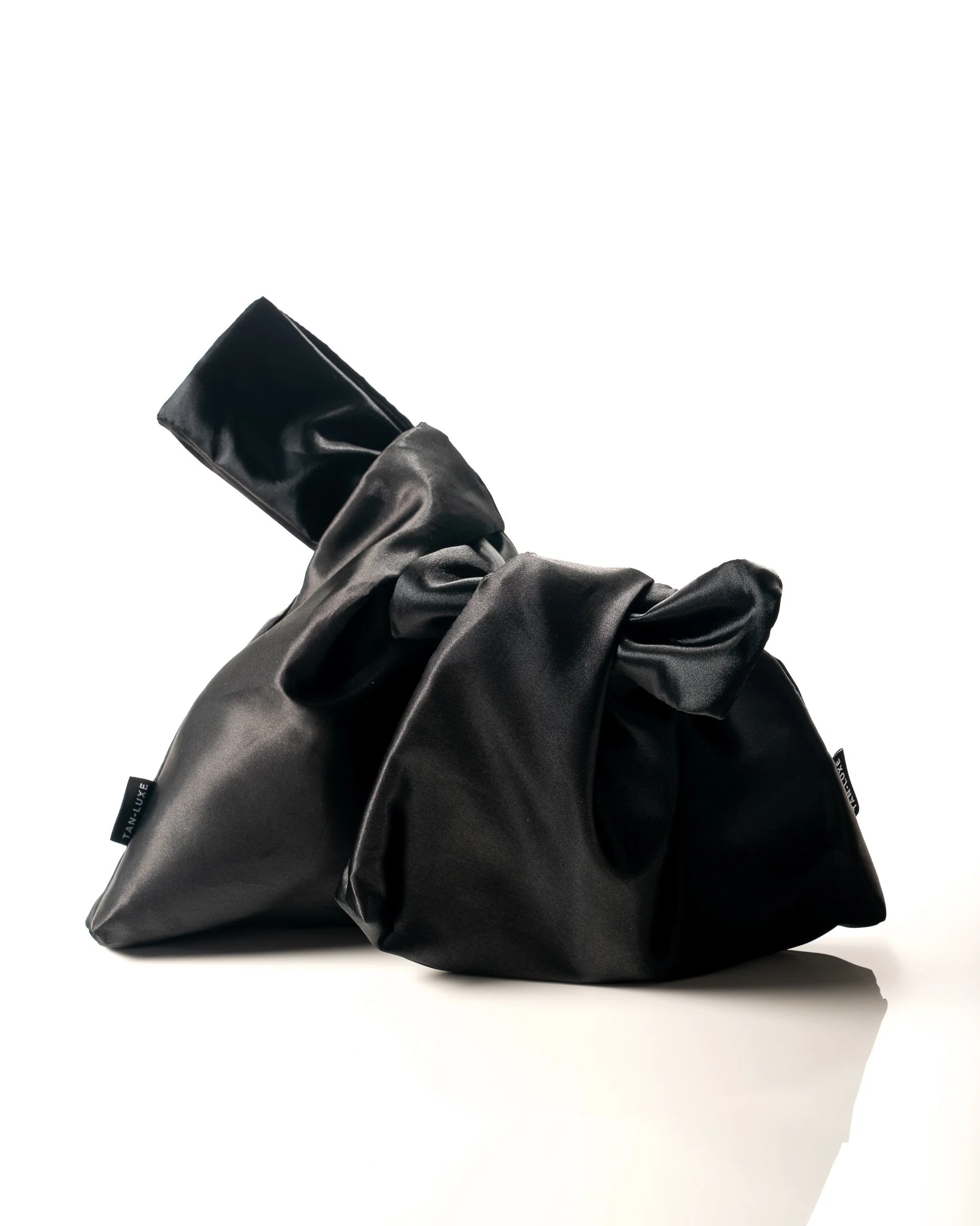 Two black satin-style handbags with large bows, one with a shoulder strap, on a white background.