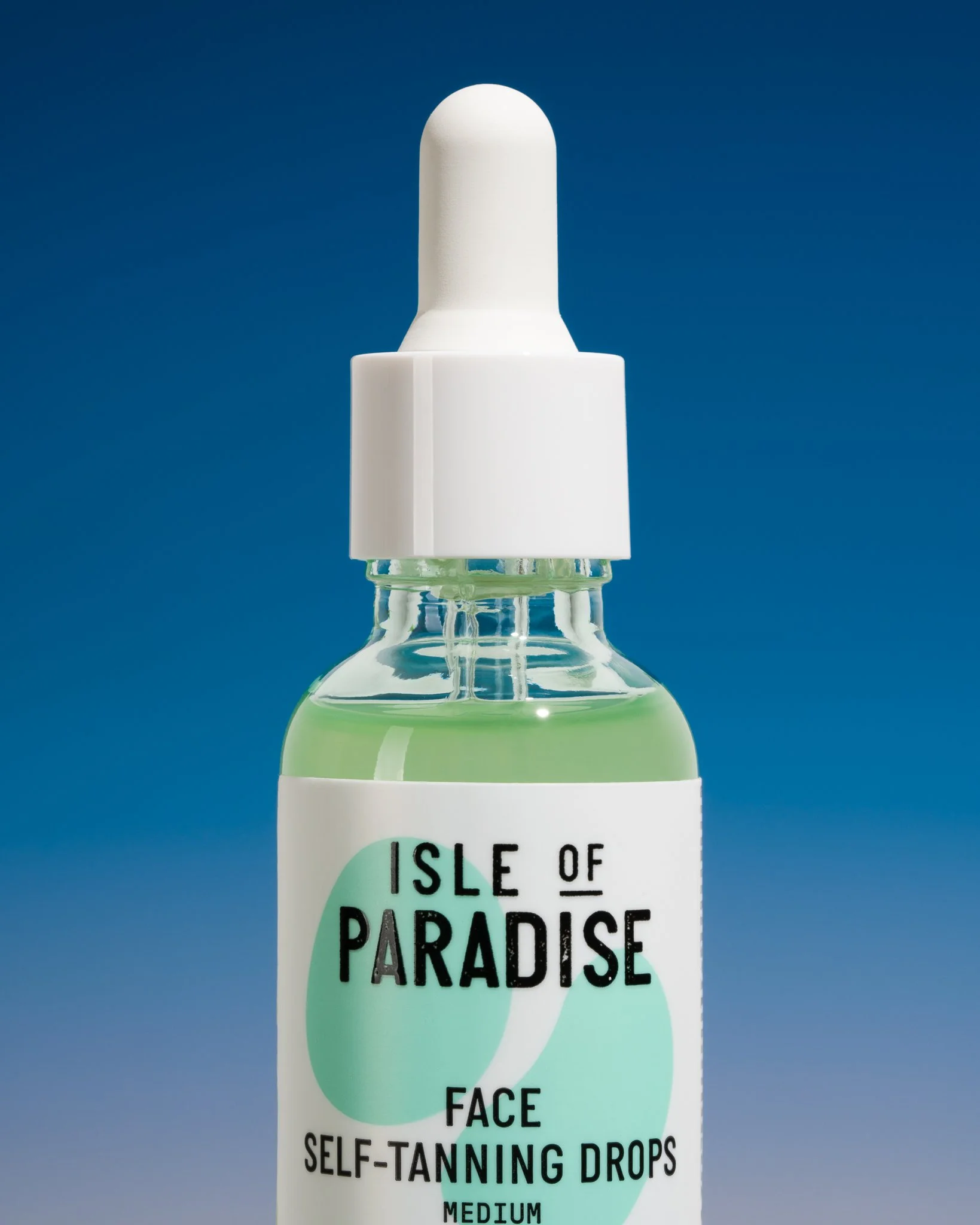 A small glass bottle with a white dropper cap, labeled 'Isle of Paradise Face Self-Tanning Drops Medium,' containing light green liquid against a blue background.