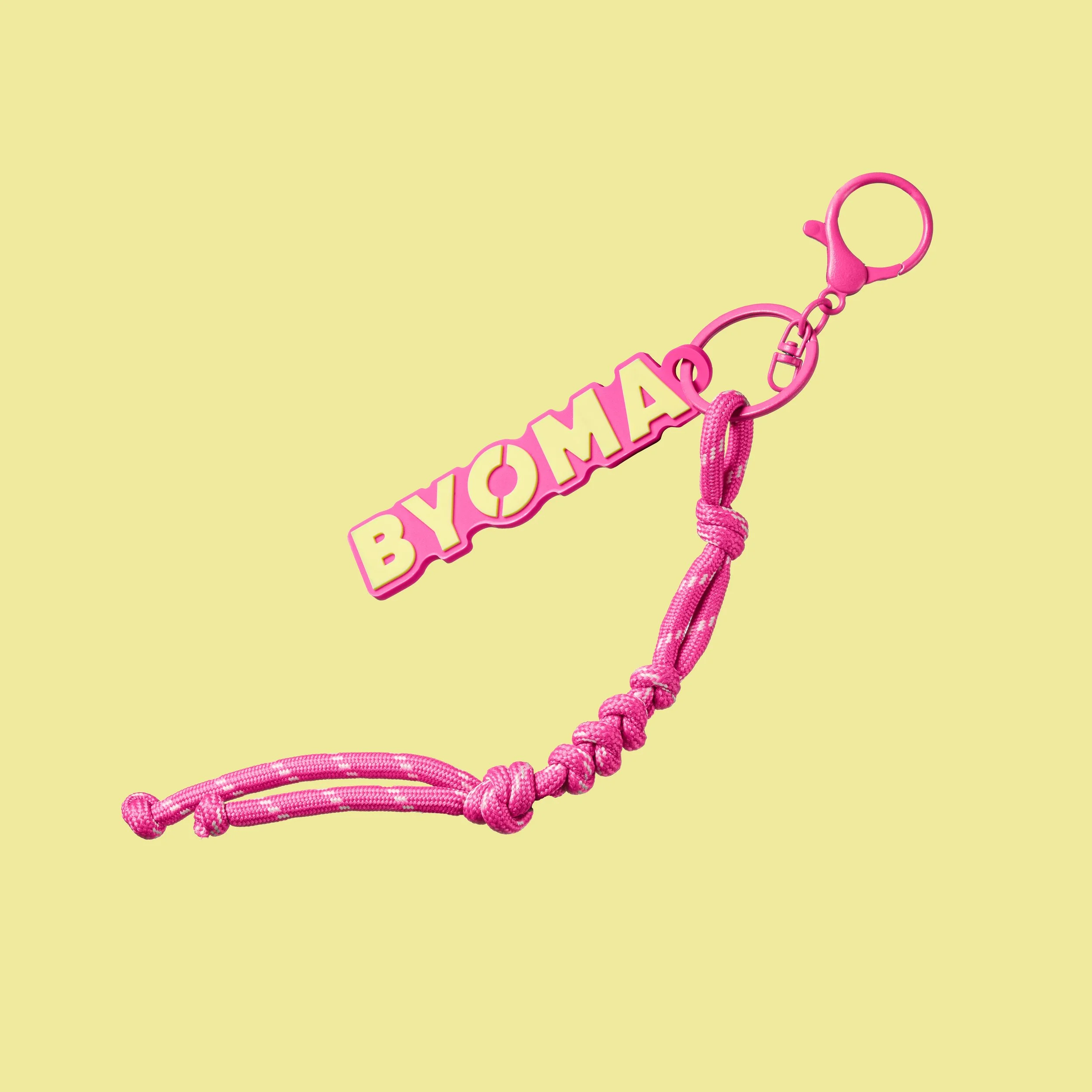 Pink keychain with a yellow background, featuring a dangling charm with text in Cyrillic script and a pink knotted rope.