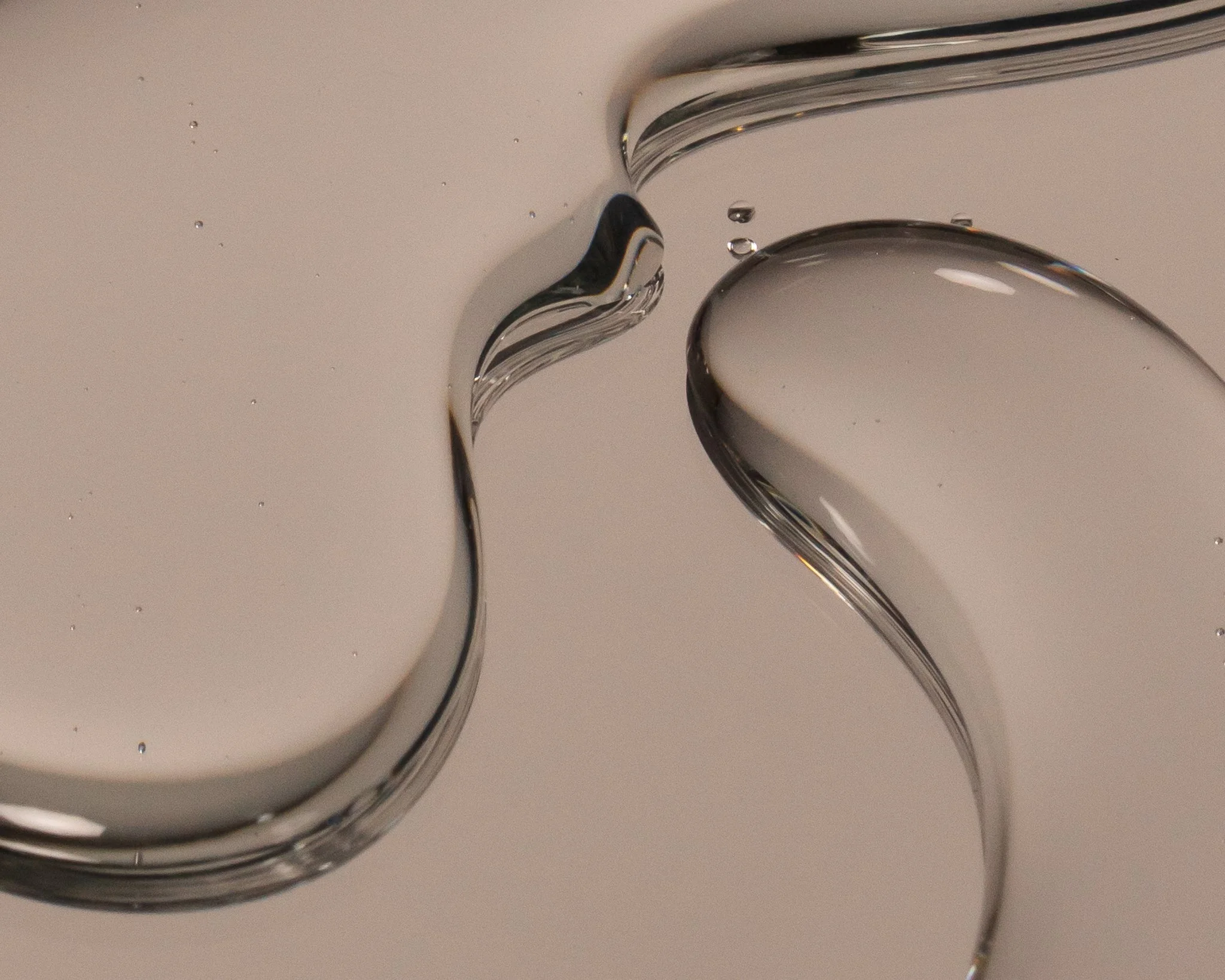 Close-up of two twisting, transparent, glass streams of liquid or gel suspended against a pale background.