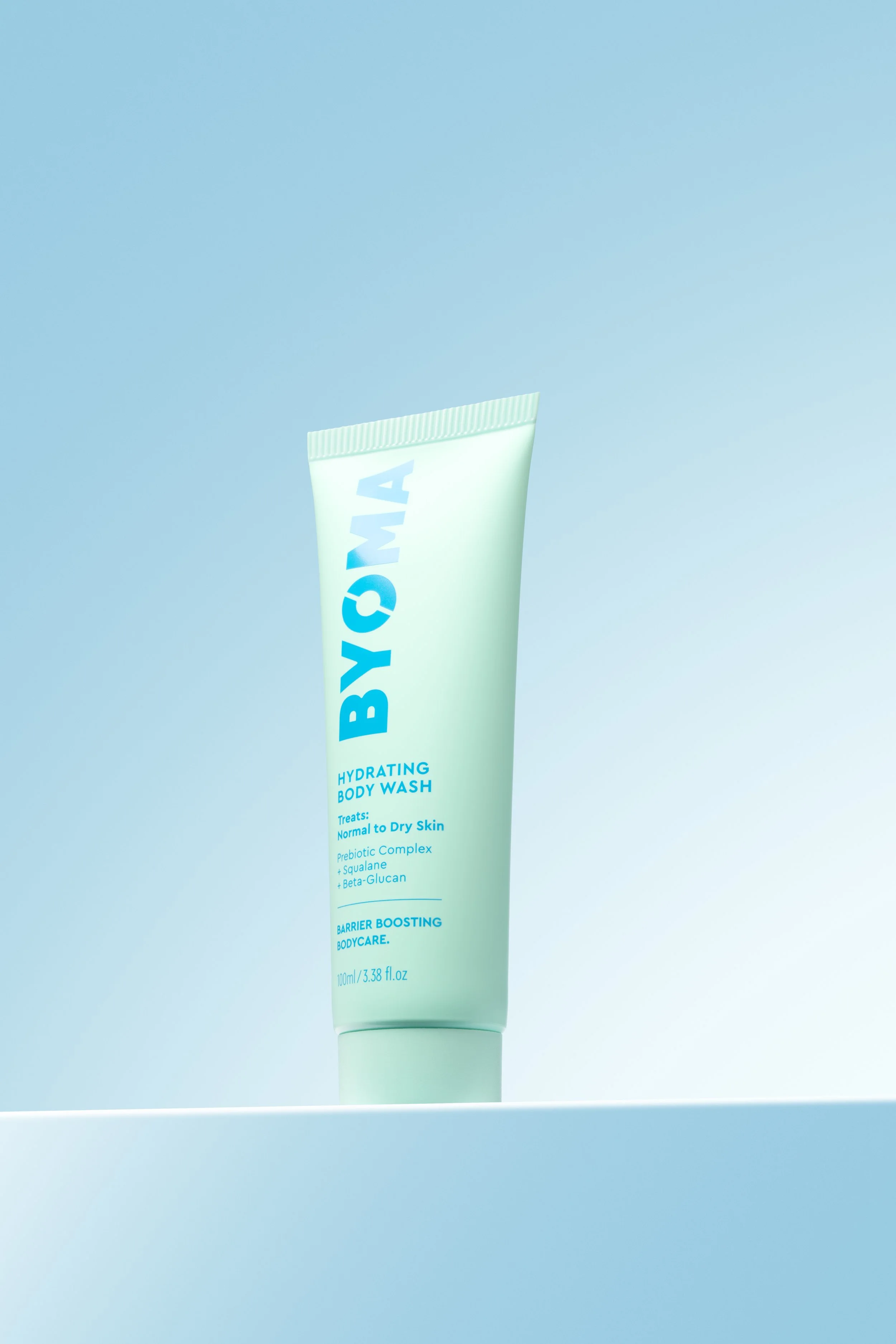 A light green tube of Byoma hydrating body wash standing on a flat surface with a blue gradient background.