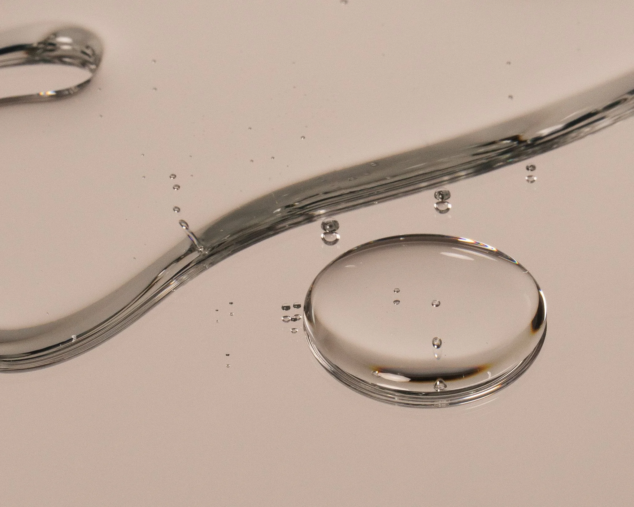Close-up of clear liquid droplet with smaller bubbles on a smooth surface