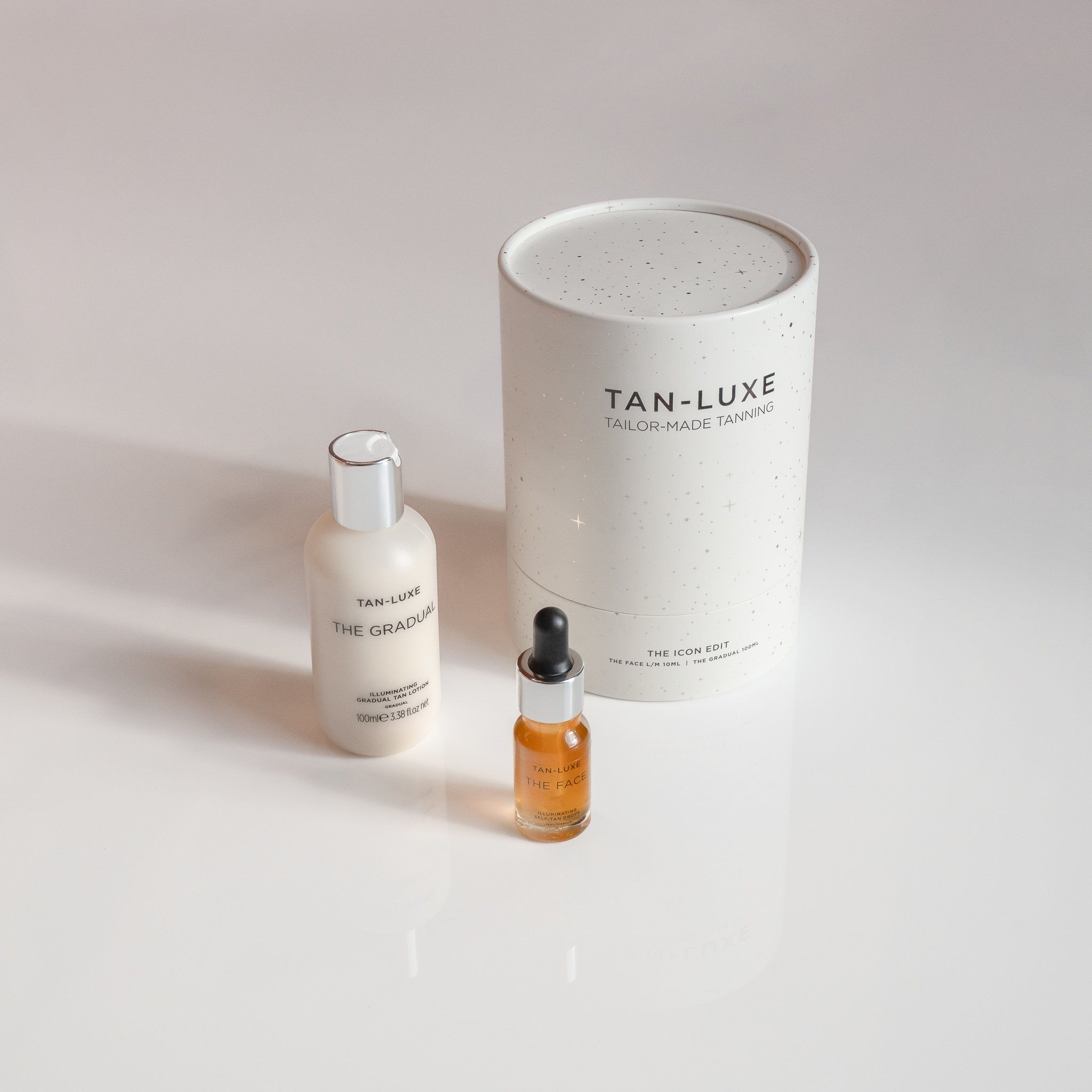 Three skincare products from Tan-Luxe, including a white bottle labeled "The Gradual," a small amber bottle labeled "The Face," and a large cylindrical container labeled "Tan-Luxe TAILOR-MADE TANNING," all on a white surface with a light background.