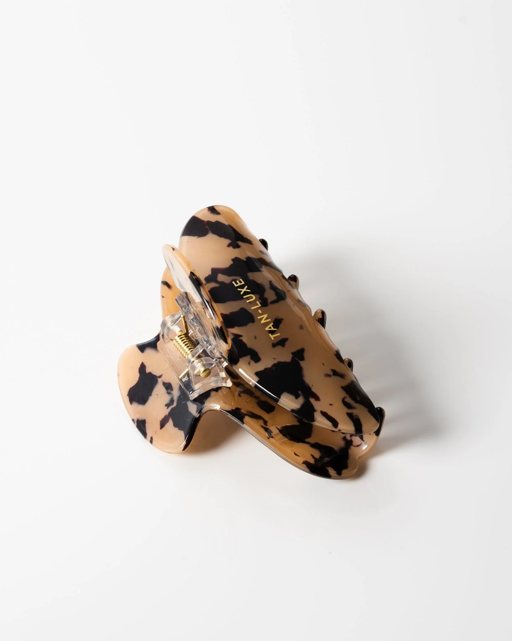 Tortoiseshell-patterned hair claw with metal spring hinge, labeled 'TAN-LUXE' on a white background.