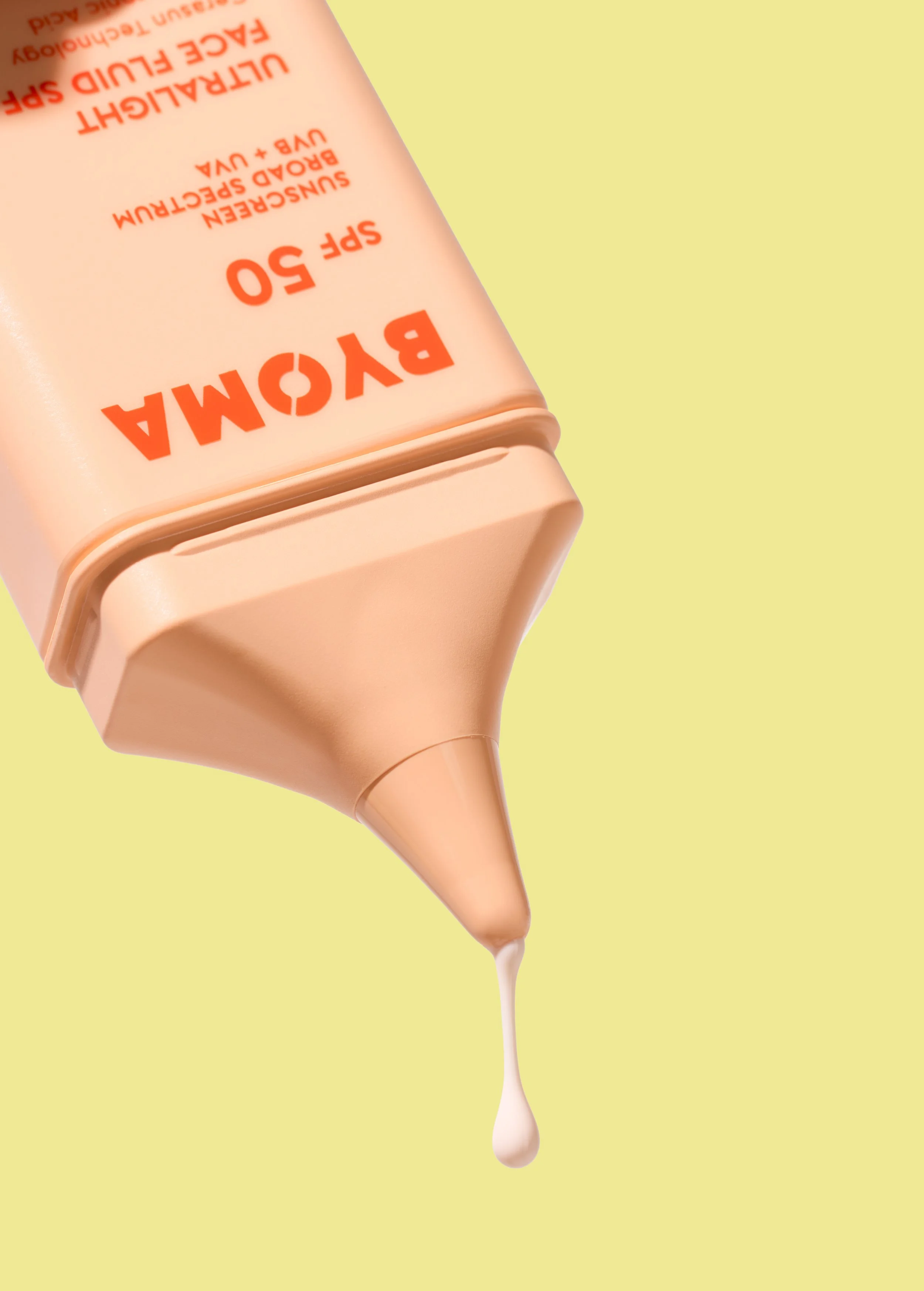 Close-up of a beige bottle of BYOMA sunscreen with a drop of lotion hanging from its nozzle against a pastel yellow background.