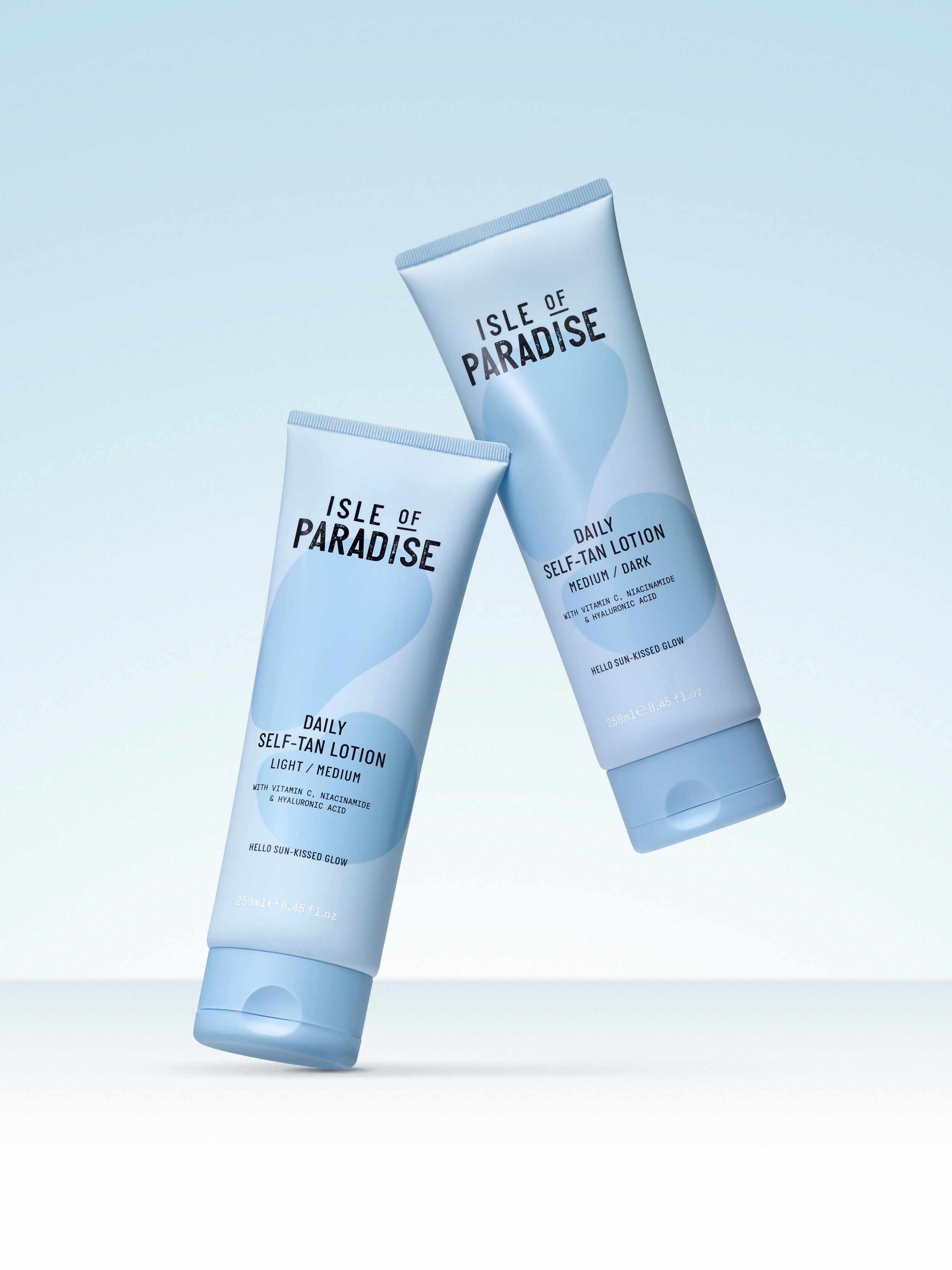 Two tubes of Isle of Paradise daily self-tan lotion, one labeled light/medium and the other dark, floating against a light blue background.