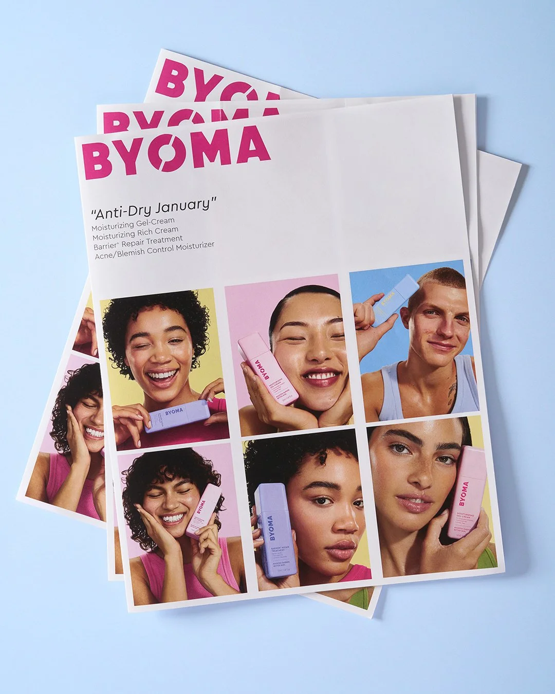 Printed promotional flyers for BYOMA skincare products featuring diverse models holding blue and pink bottles, with product descriptions and branding on a light blue background.
