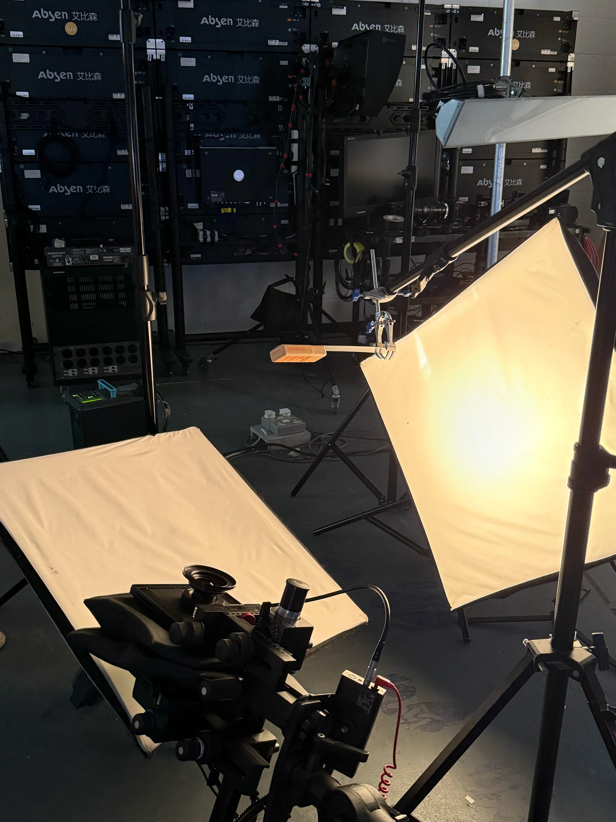 Photography studio setup with two softbox lights, a camera on a tripod, and a backdrop in a room with server racks in the background.