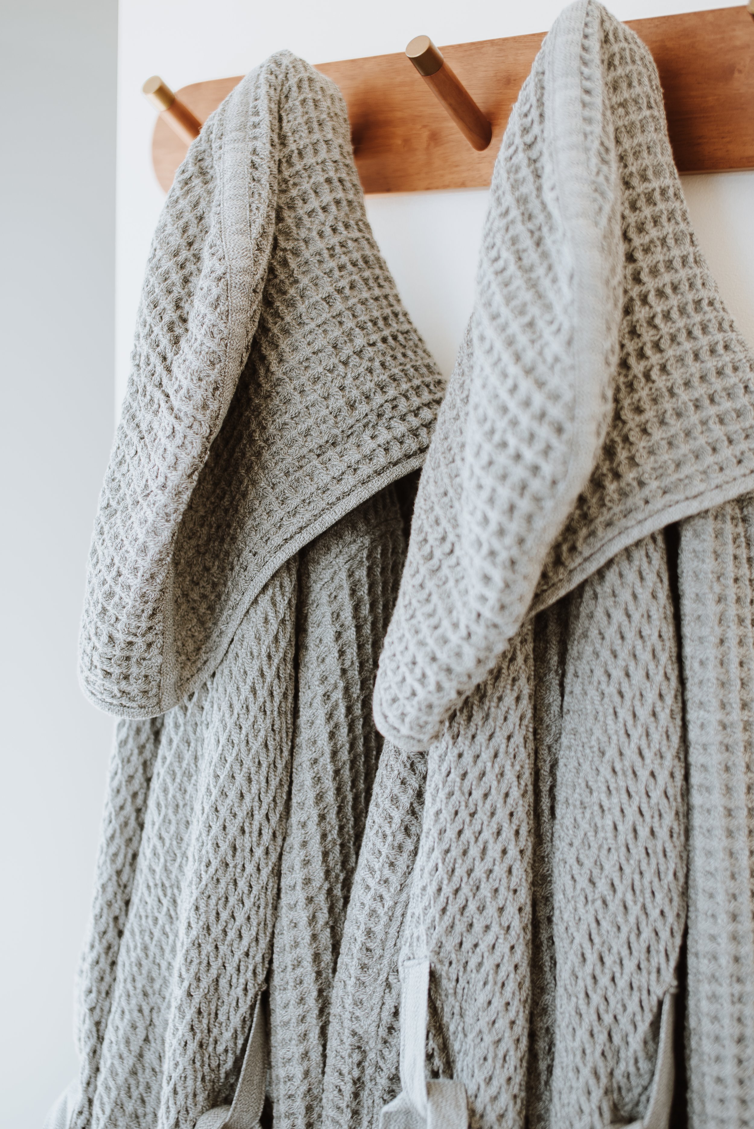 Two beige, textured bathrobes hanging on a wooden rack.