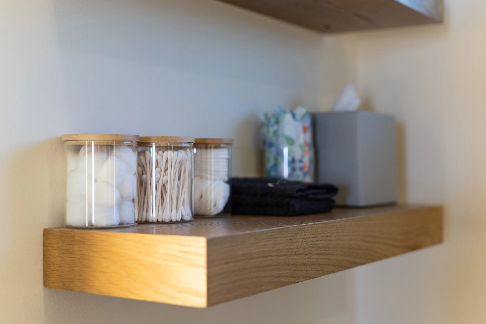 A wooden shelf holding cotton balls, cotton swabs, and tissues in containers.