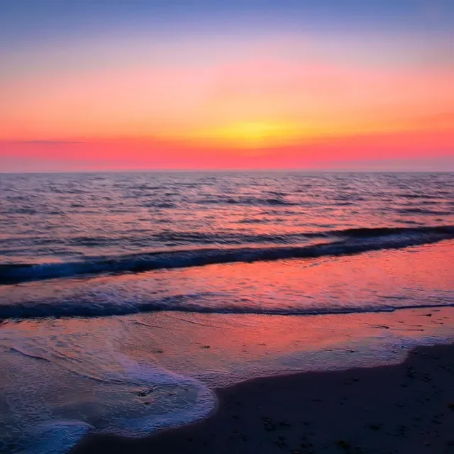 Ein Sonnenuntergang über dem Meer, der Himmel in Pastellfarben, Wellen am Strand