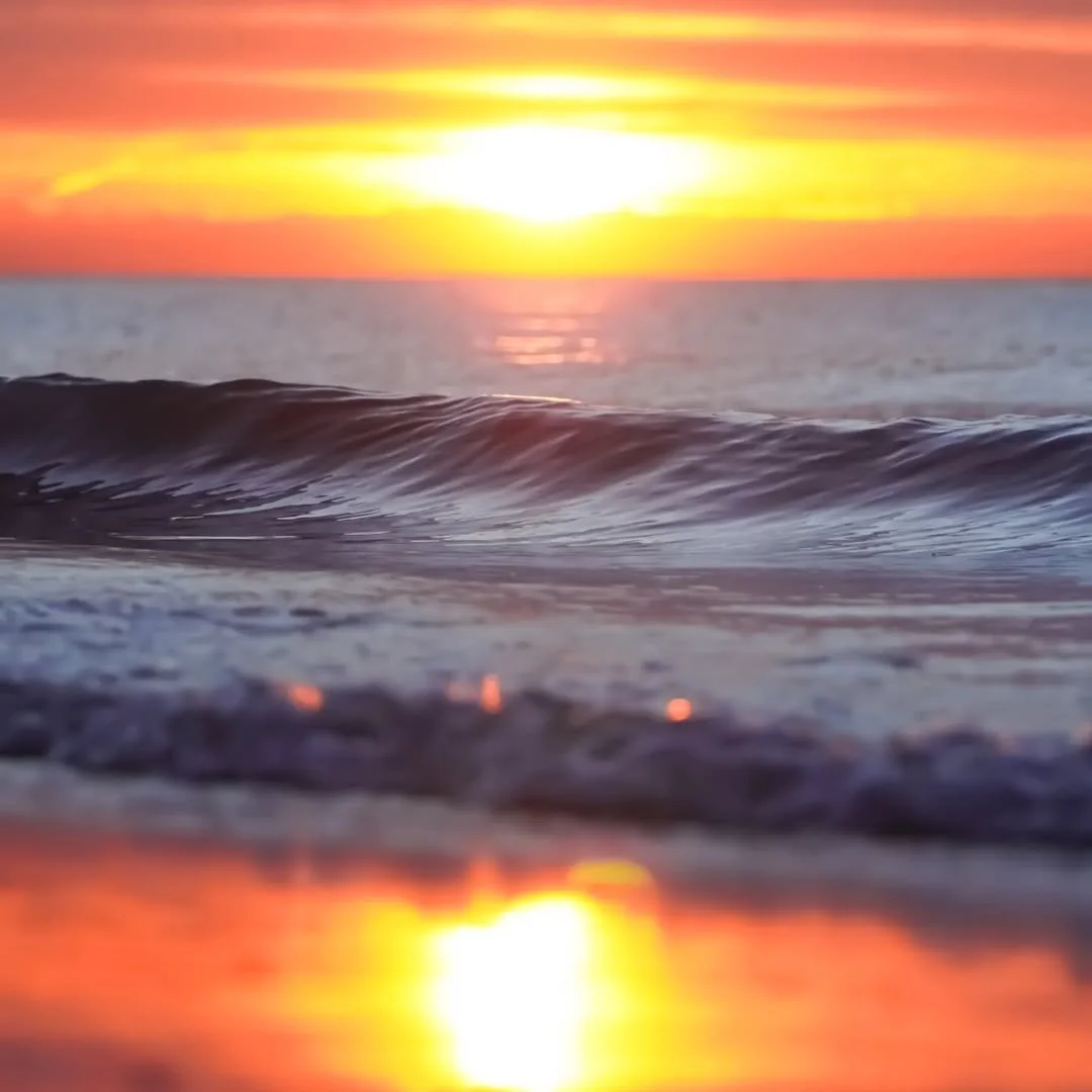 Sonnenuntergang über dem Meer mit Wellen im Vordergrund.
