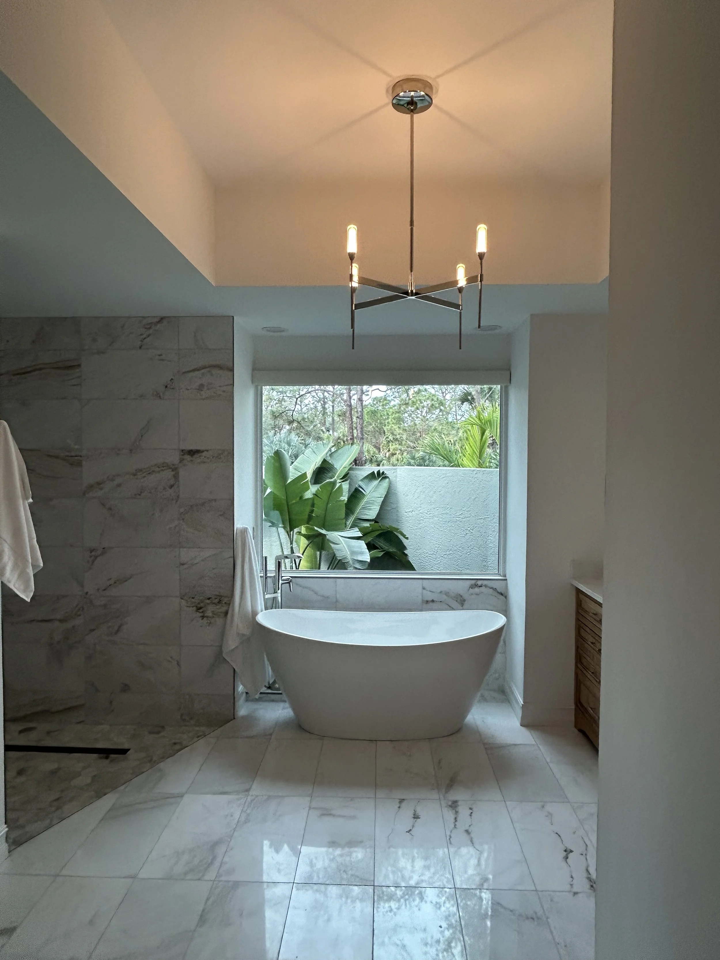 Interior Design Project: Minimal and Organic Bathroom remodel featuring tall potted tree with dense green leaves in a large beige pot, illuminated from behind against a plain light-colored wall, with a small wooden bench.