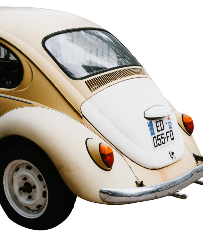 Close-up of the rear end of a vintage cream-colored Volkswagen Beetle, showing the taillights, rear window, license plate, and bumper.