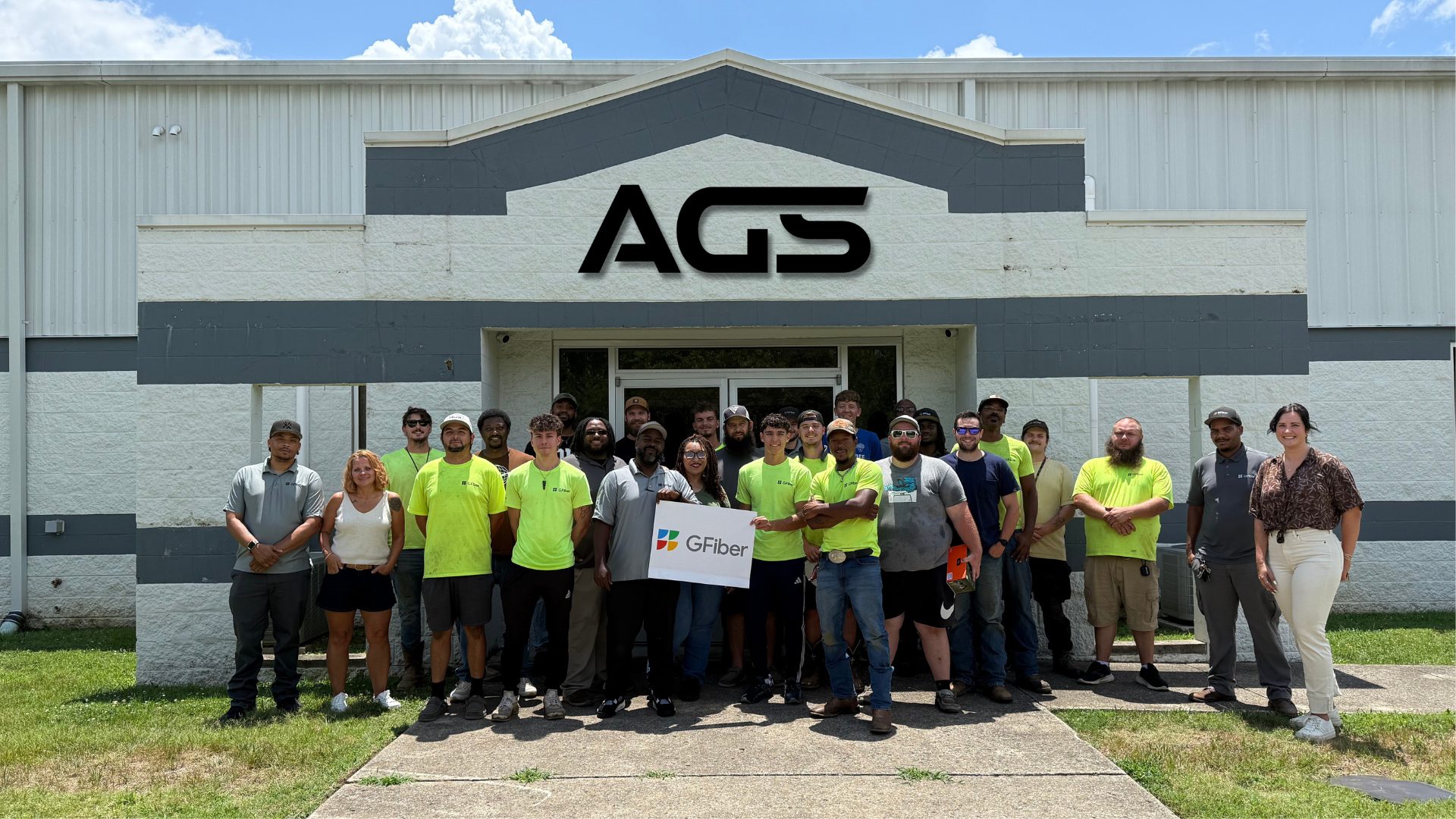 Group of diverse people standing outside the AGS building, holding a GFiber sign, with some wearing neon green shirts.