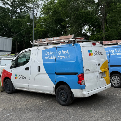 G Fiber service van parked in a lot with trees in the background, displaying the slogan 'Delivering fast, reliable internet'.