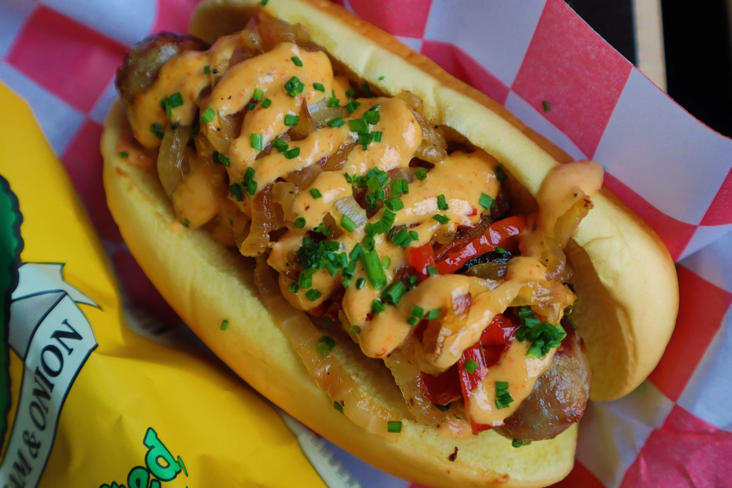 Hot dog topped with chopped onions, red peppers, and chives in a bun