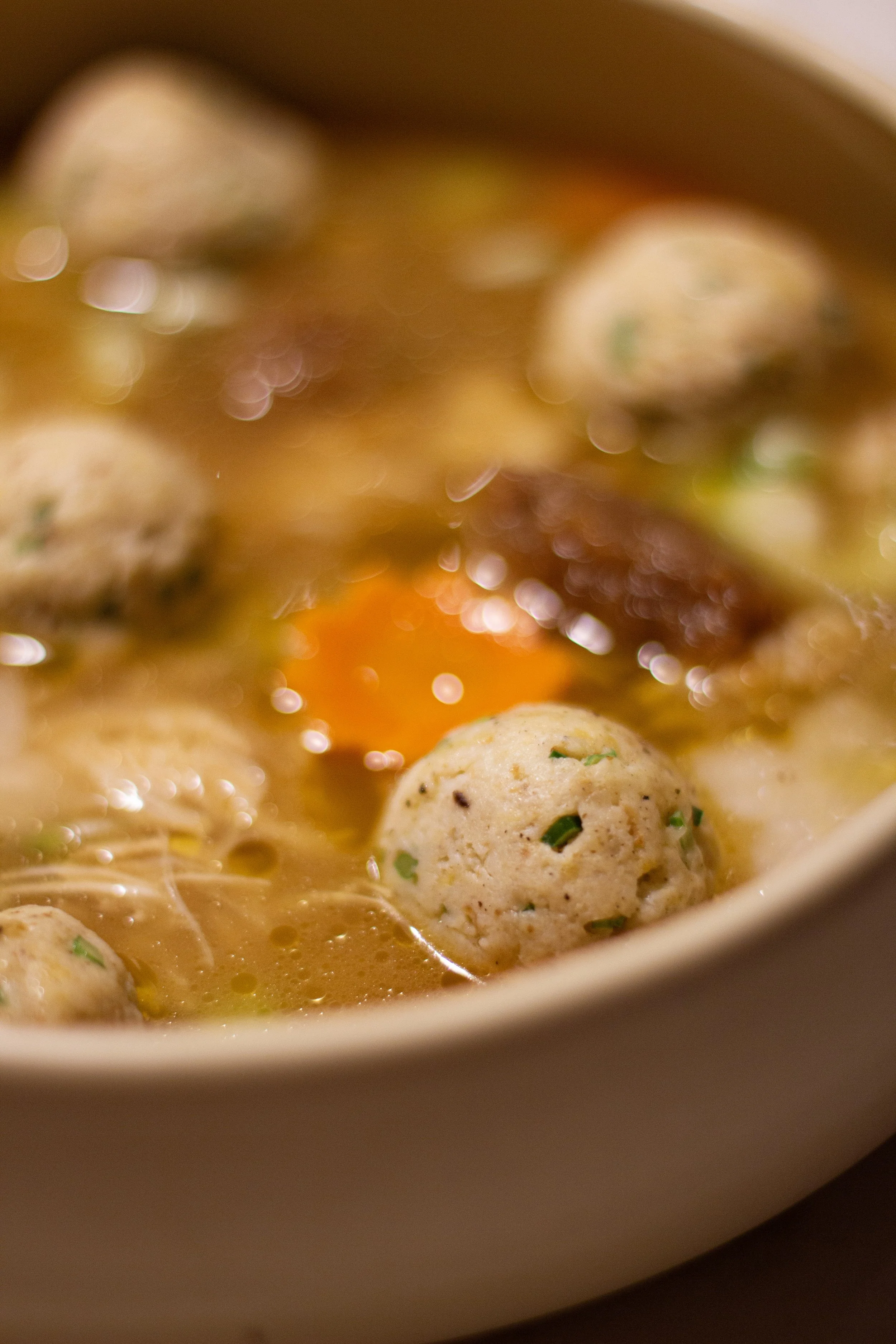 Close-up of a bowl containing soup with meatballs, an egg yolk, and broth, garnished with herbs.
