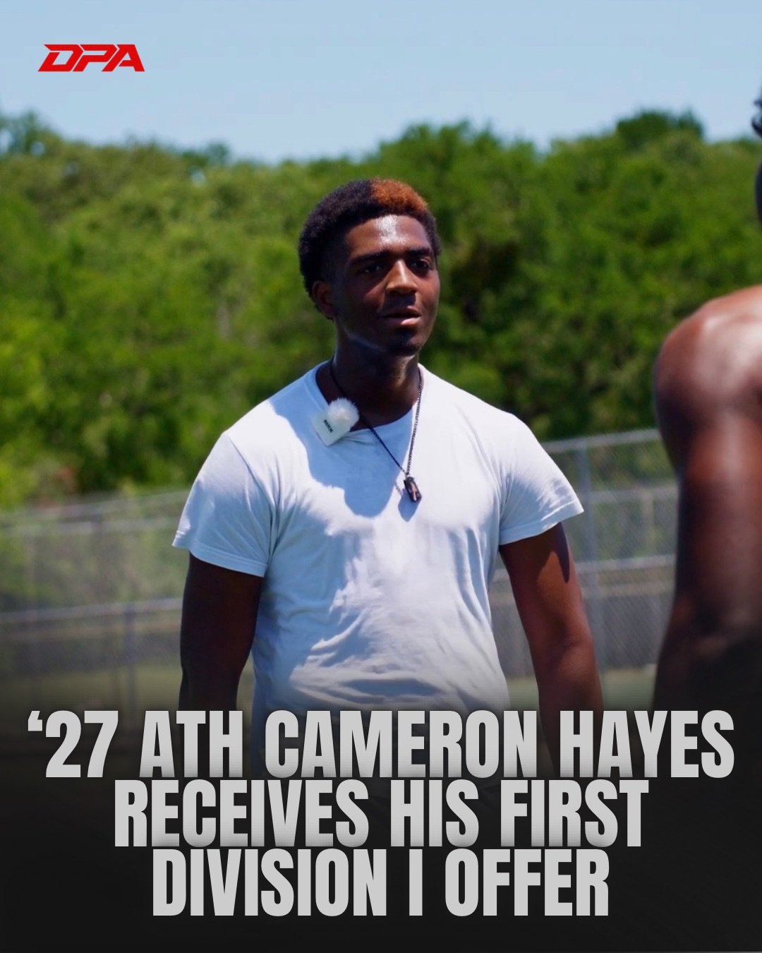 A young man with short hair wearing a white t-shirt and a necklace, standing outdoors during daytime with a background of green trees, with text overlay about Cameron Hayes receiving his first division offer.