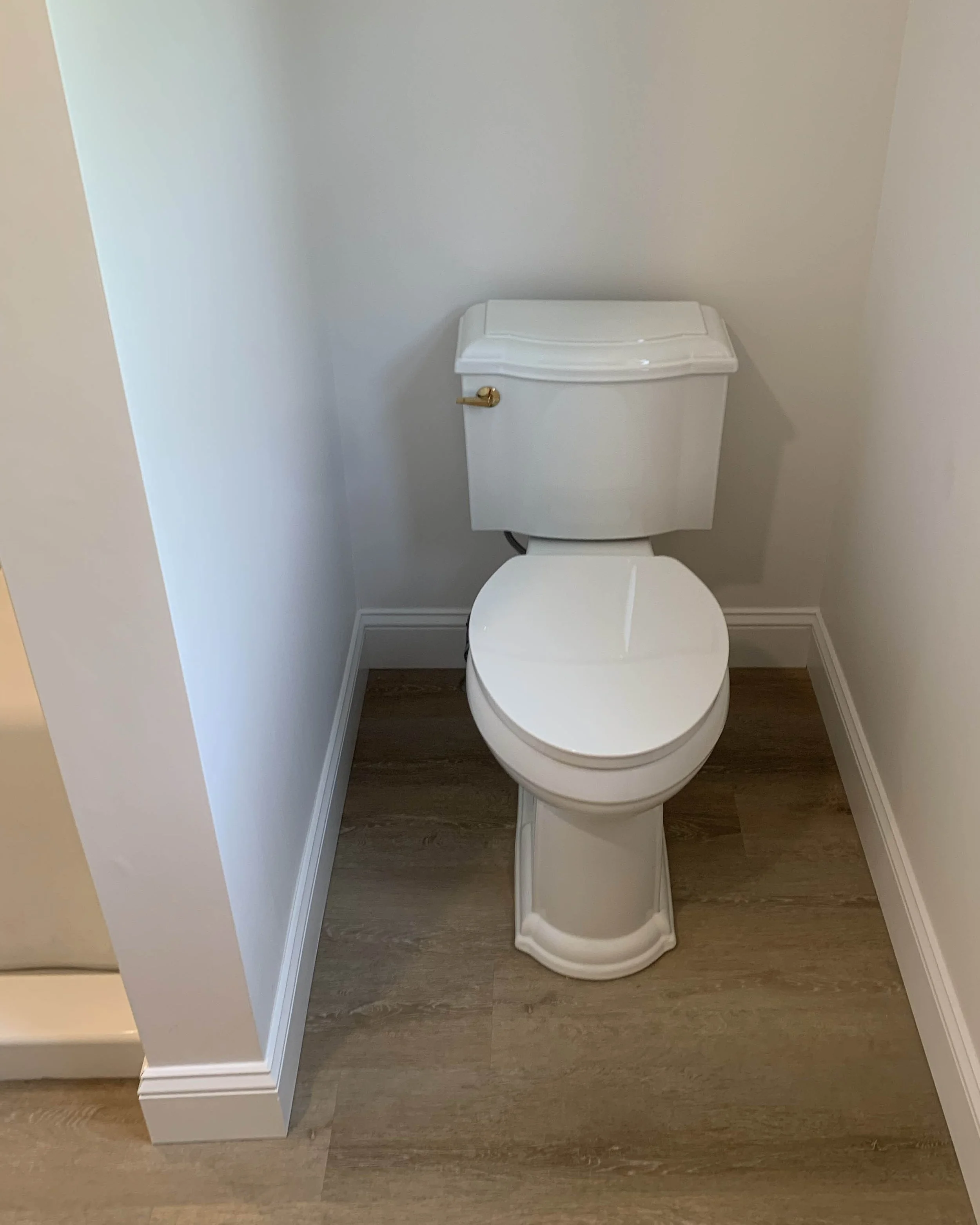 A white toilet with a closed lid in a small bathroom with white walls and wooden flooring.