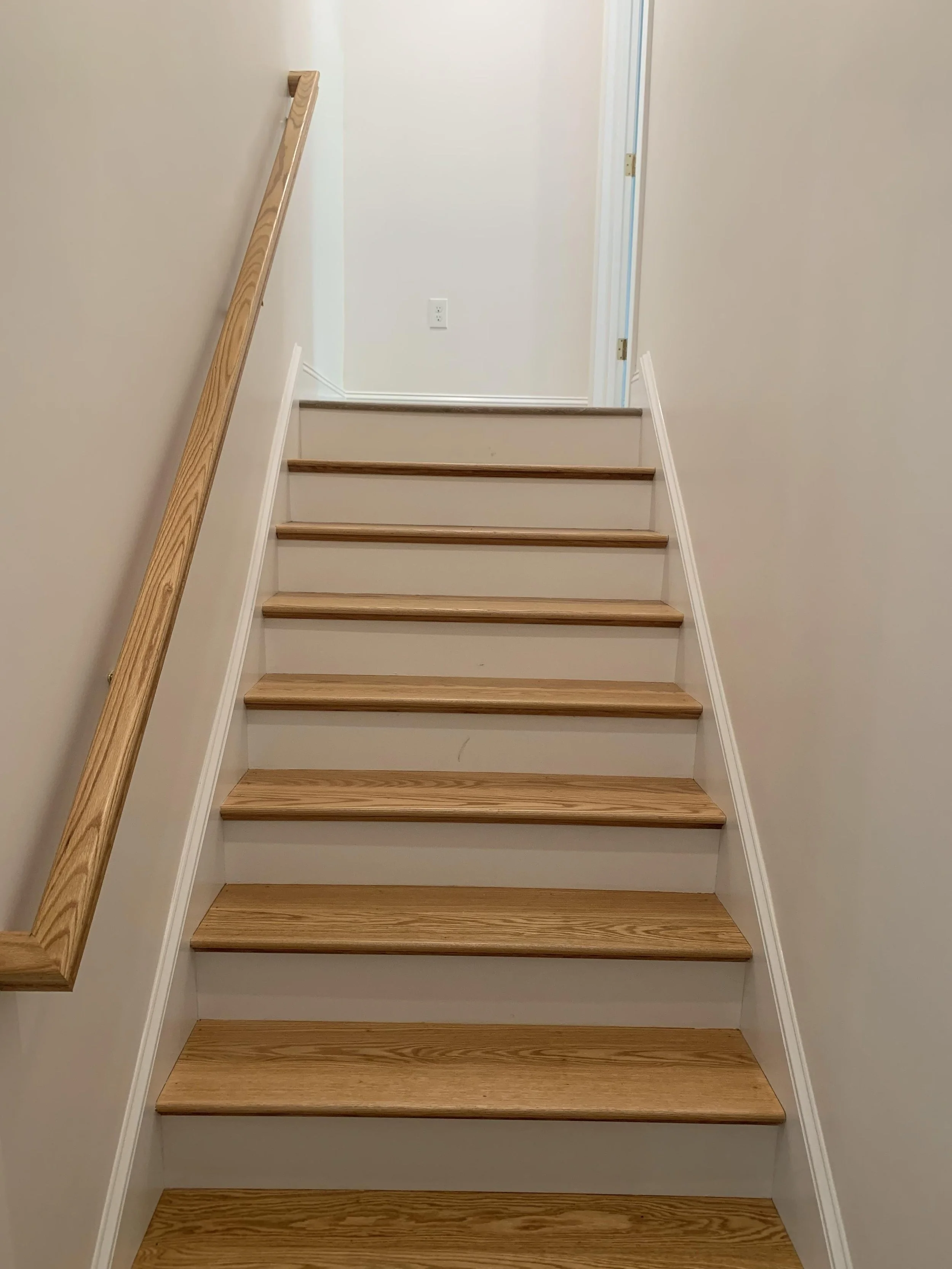 Wooden staircase with a handrail on the left side, leading up to a doorway in a residential home.