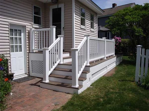 Back porch with white railing and stairs leading to a lawn with flowers and trees.