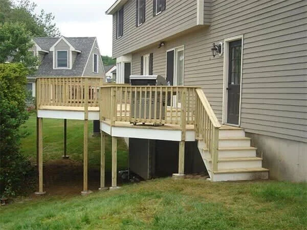 New wooden deck attached to the back of a beige house, with stairs leading down to the yard.