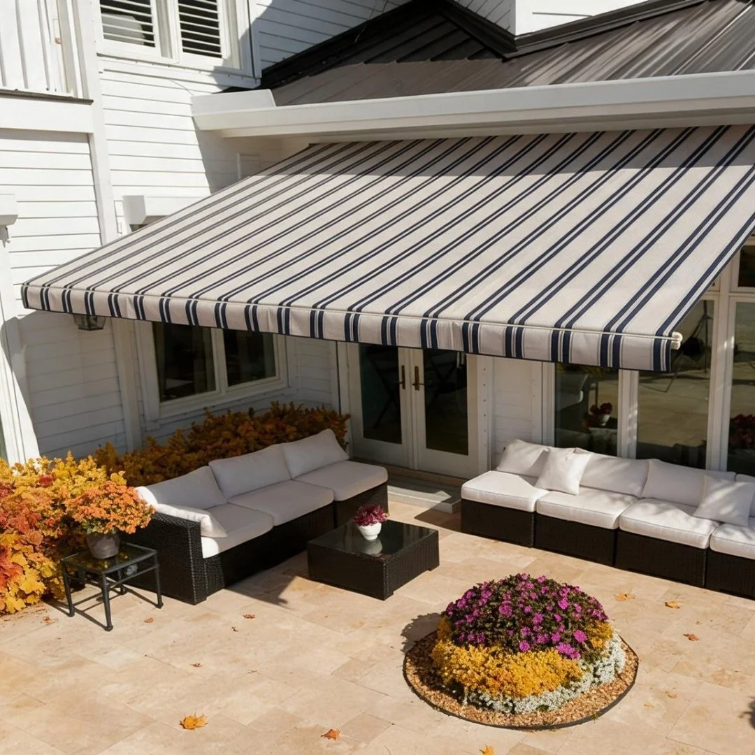 Patio area with outdoor sofa seating under a striped retractable awning, surrounded by potted flowers and autumn foliage.